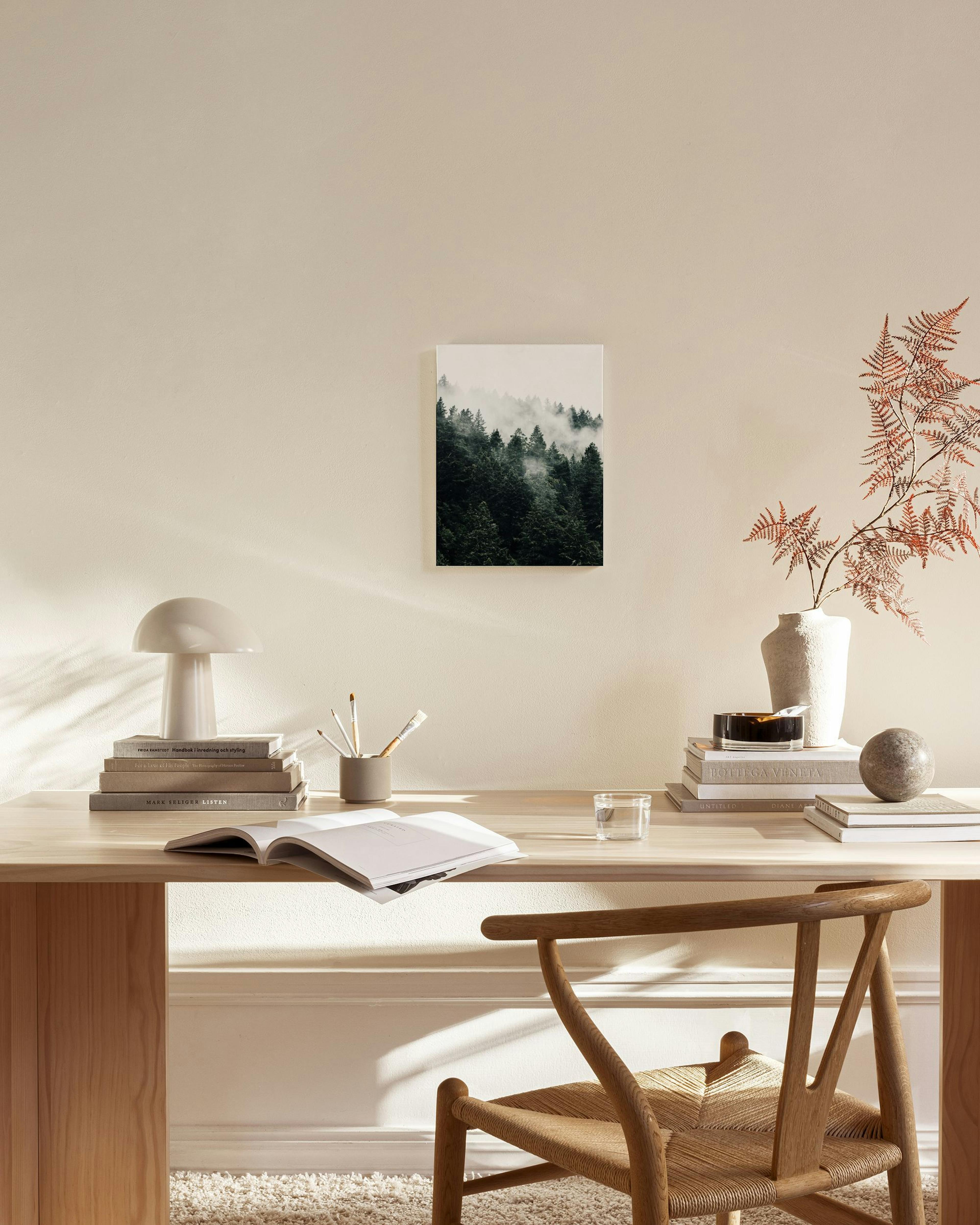 A canvas print of a misty evergreen forest, hanging on a beige wall in a minimalist living room.