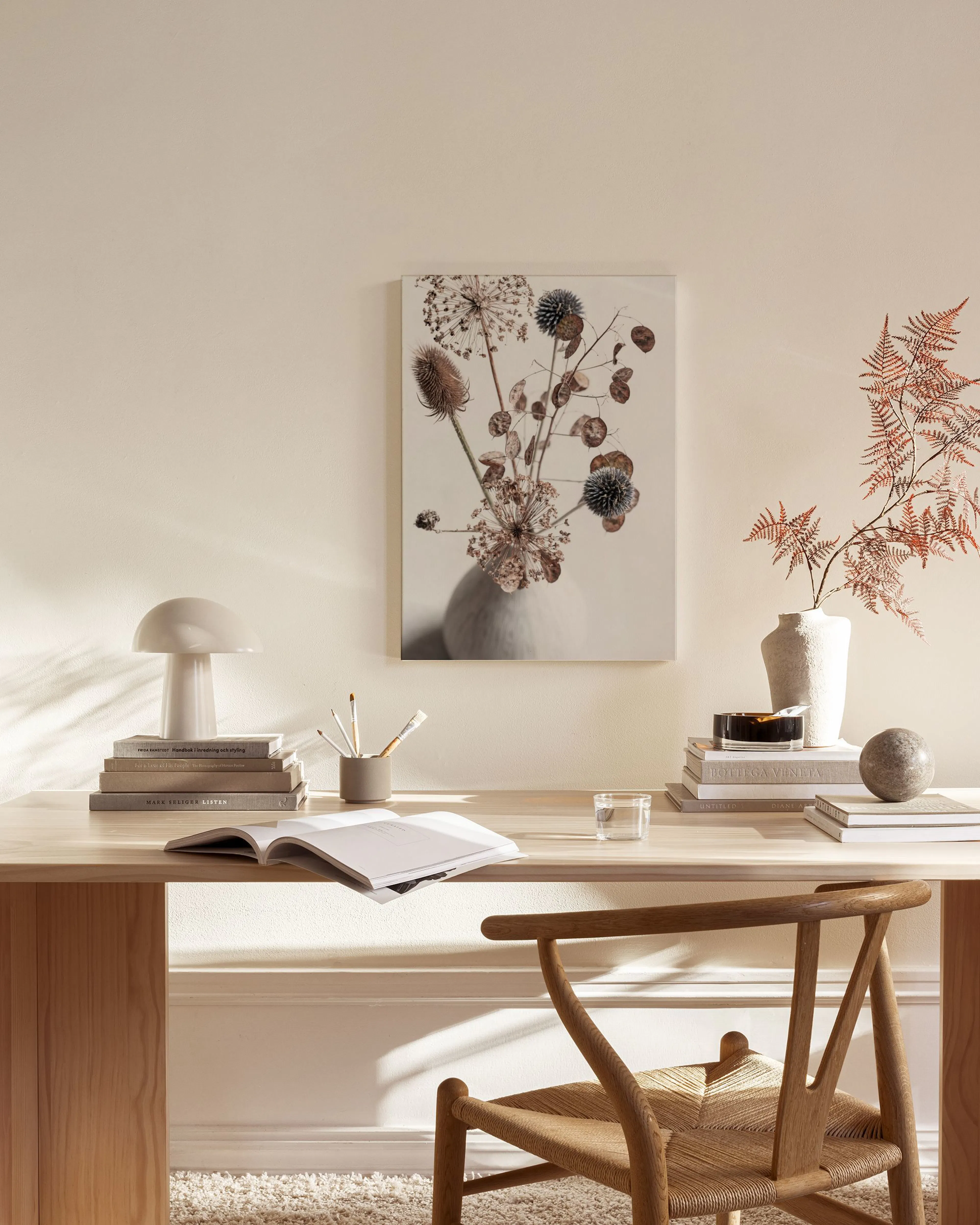 Stampa su tela di fiori secchi in un vaso, appesa sopra una panca in legno in un salotto moderno.