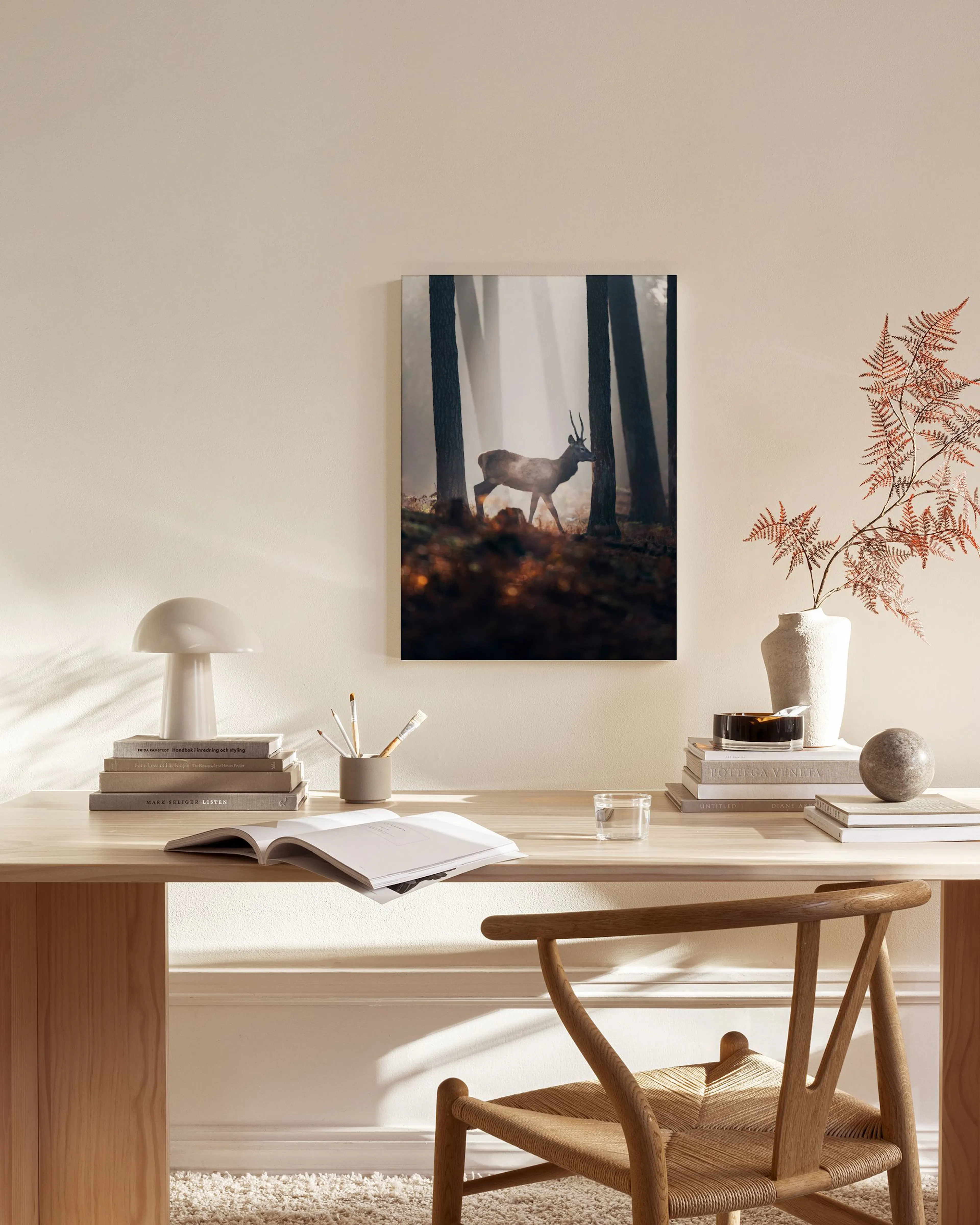 A canvas print of a deer in a foggy forest, hanging above a wooden console table in a minimalist living room.