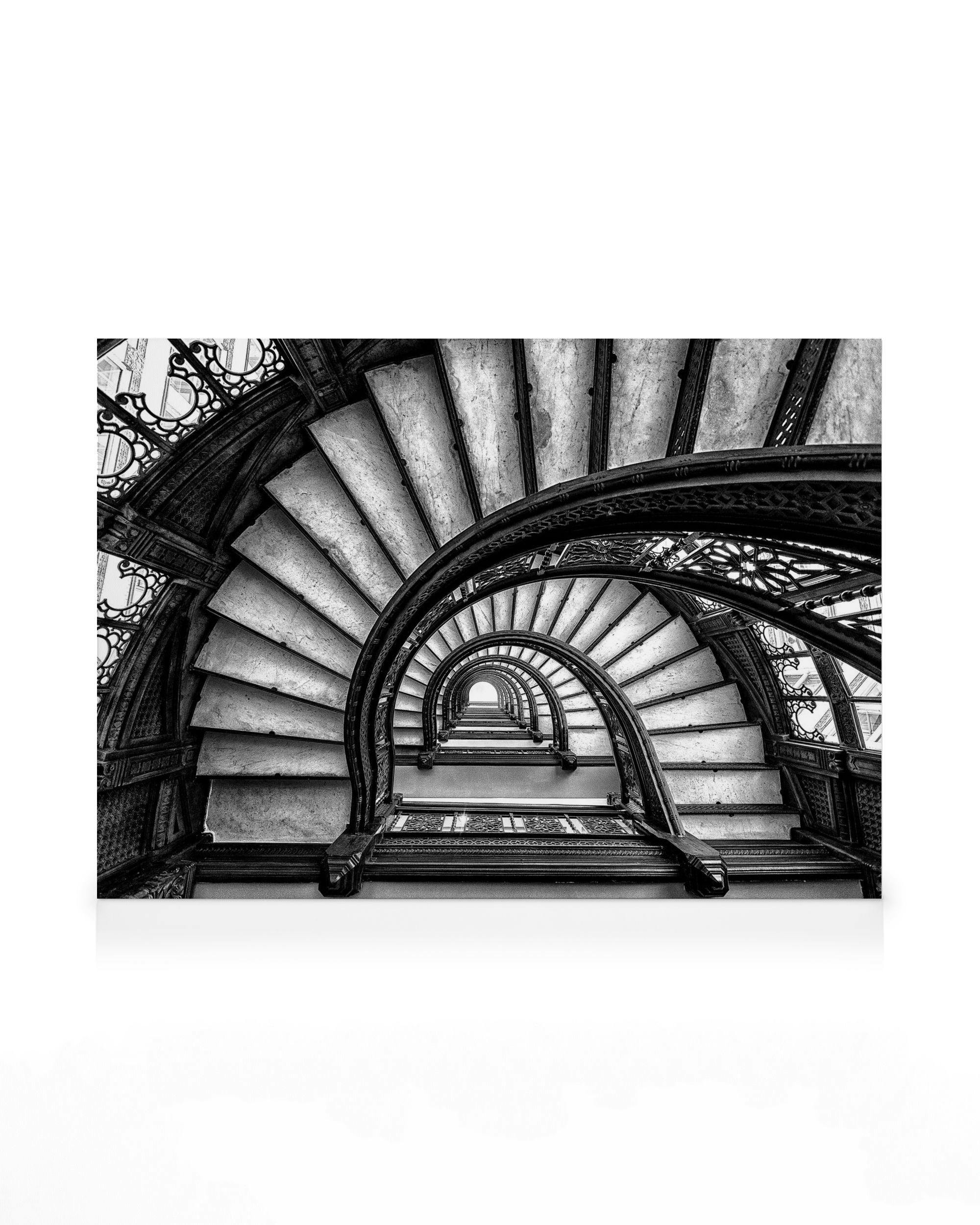 Black and white spiral staircase canvas print with repeating arches and ornate railings, creating a mesmerizing pattern.