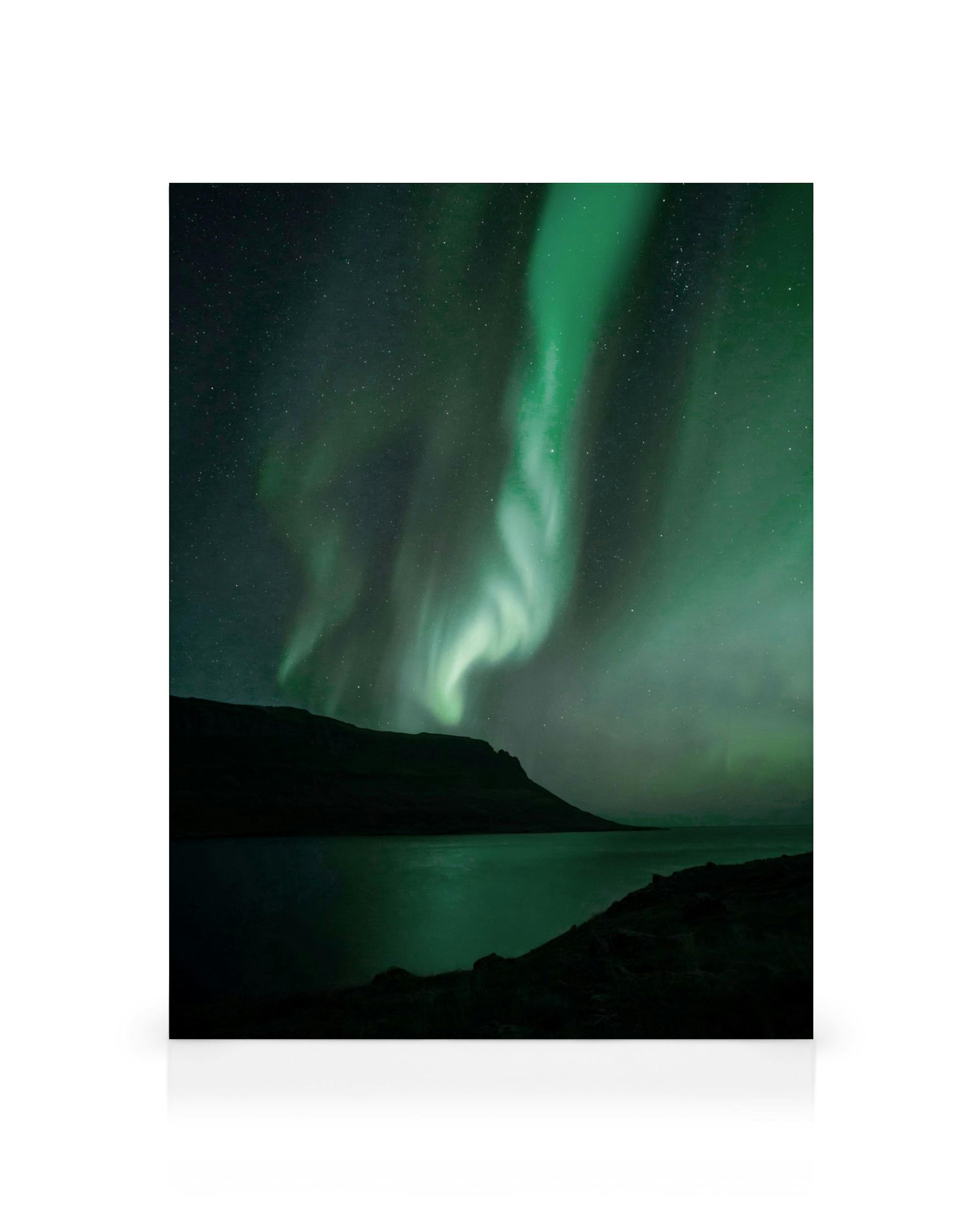 Vibrant green Northern Lights illuminate a starry sky over a dark fjord and mountains in an Iceland canvas print.