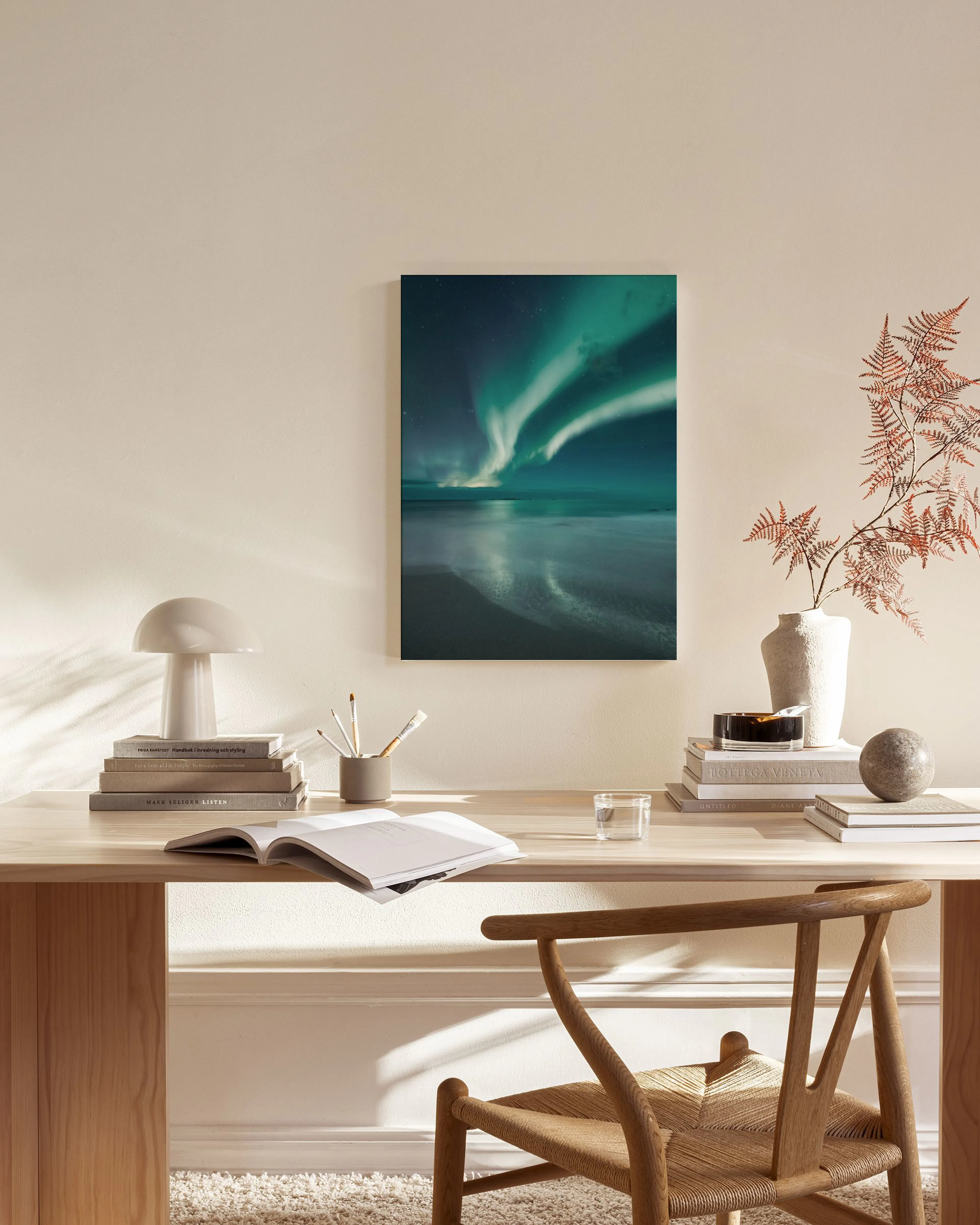 Een canvas met noorderlicht boven een wateroppervlak en strand, hangend in een neutrale woonkamer.