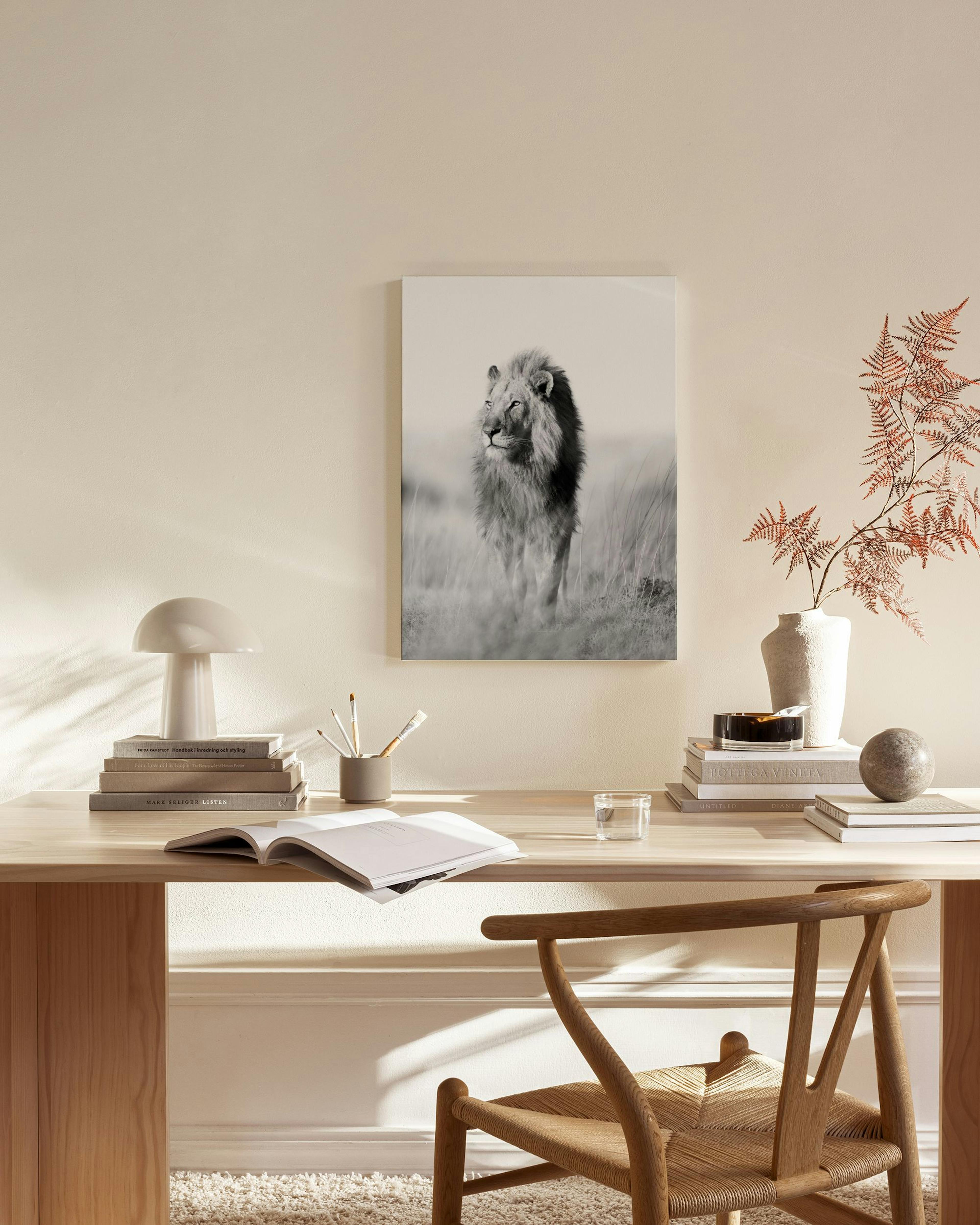 Black and white canvas print of a majestic male lion in tall grass, hanging in a minimalist living room.