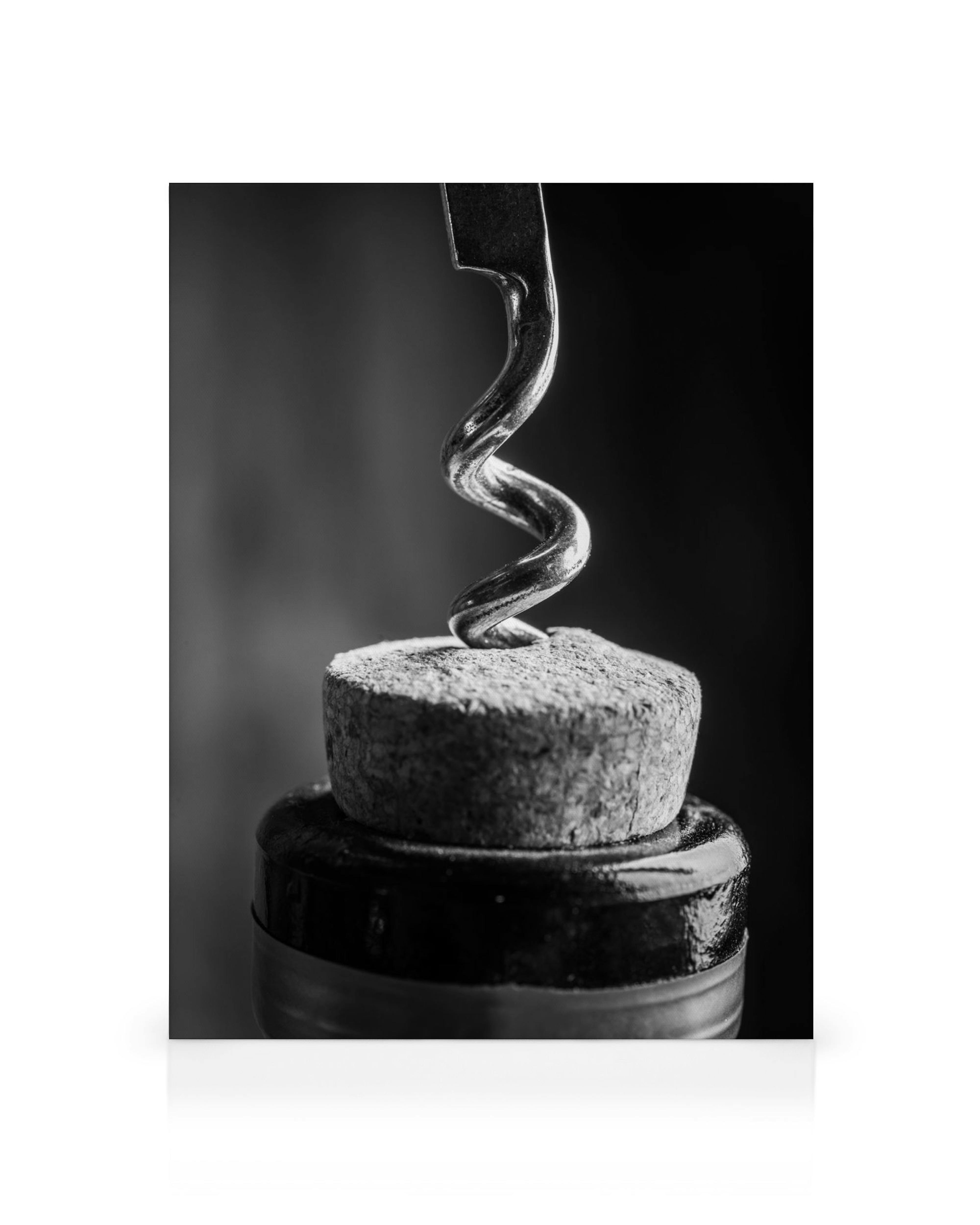 Black and white corkscrew entering a wine bottle cork, close-up, minimalist still life, kitchen art.