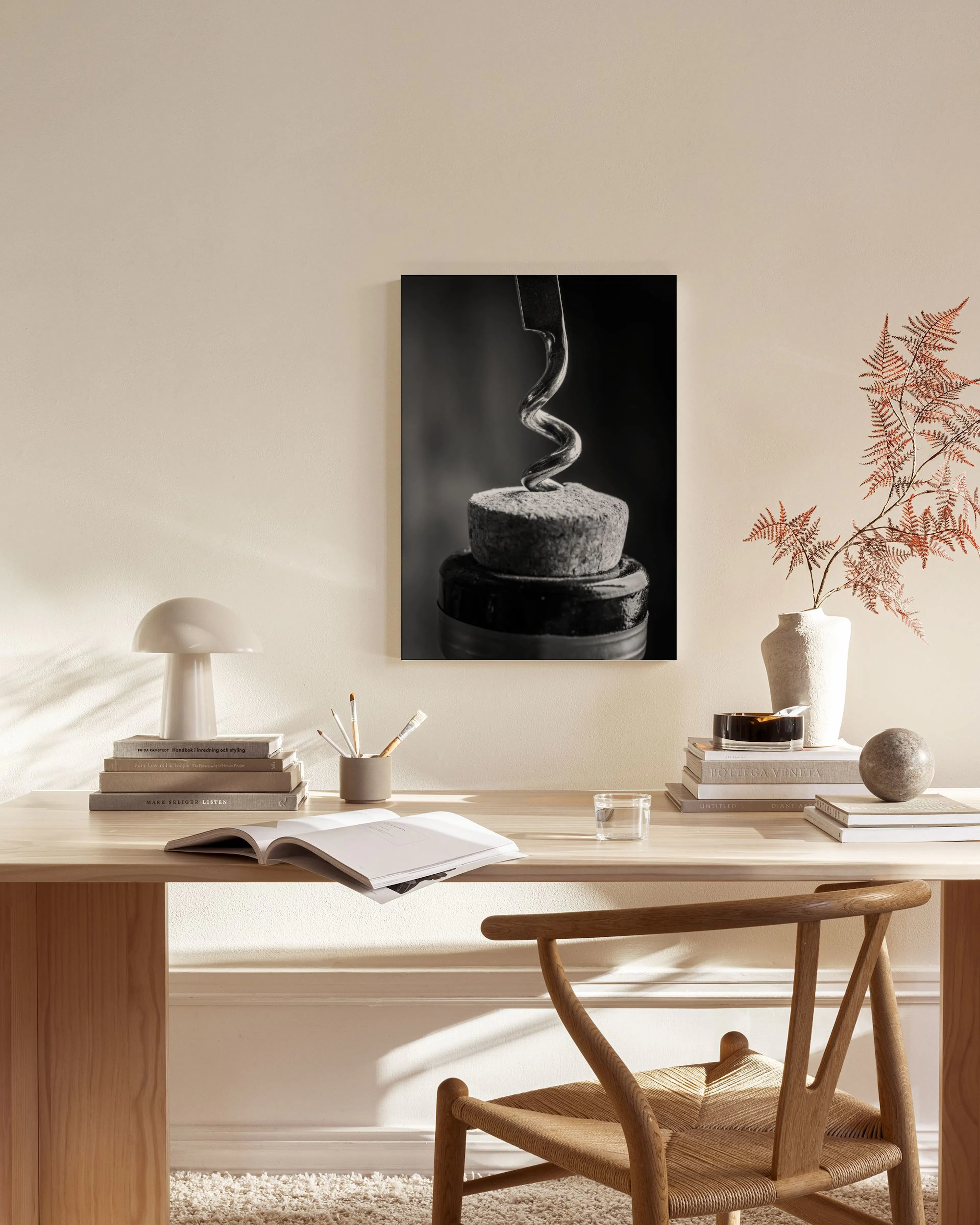 A monochrome canvas print of a corkscrew in a wine bottle, displayed in a minimal living room above a wooden console.