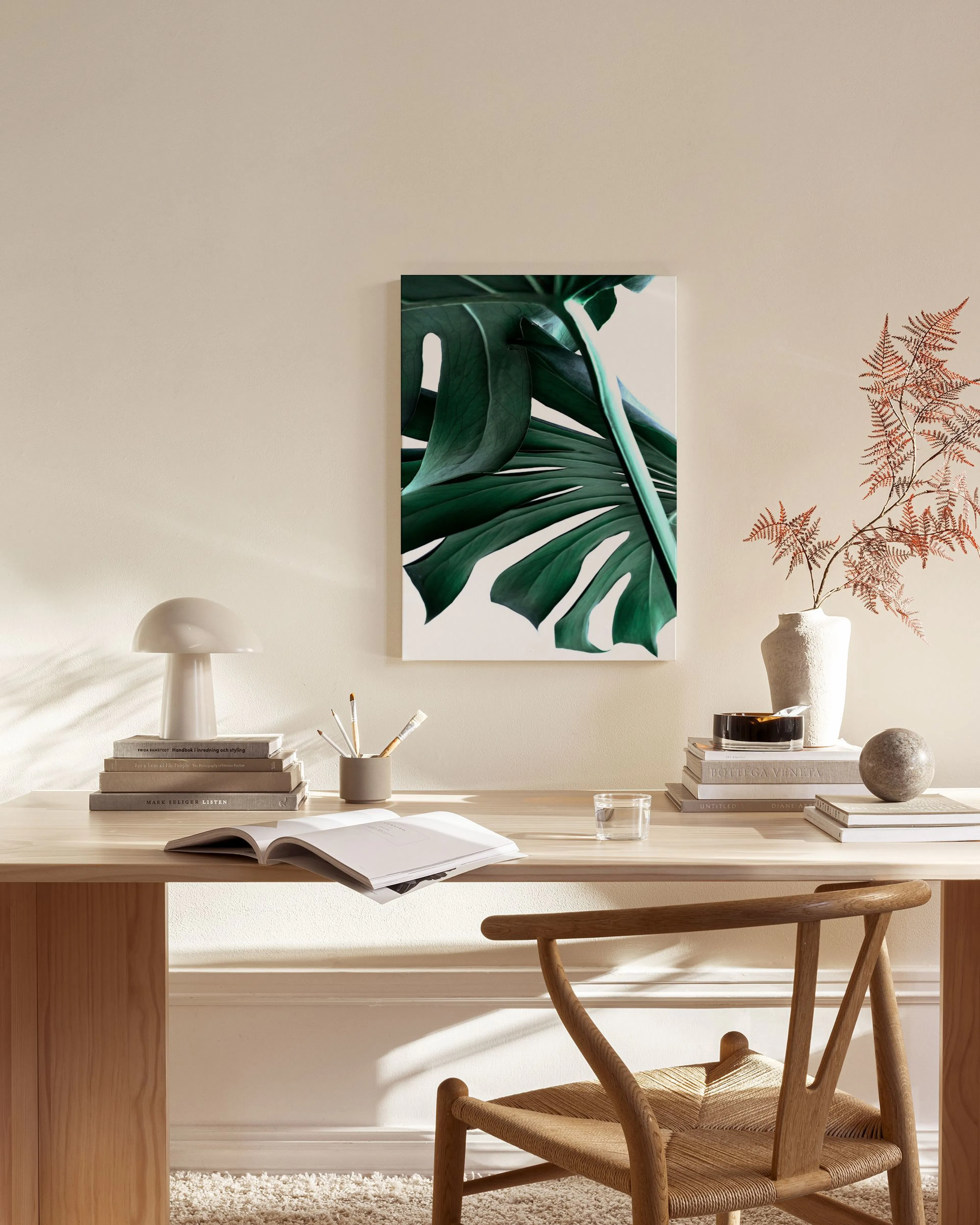 A canvas print of a large green monstera leaf on a white background, hanging in a minimalist living room.
