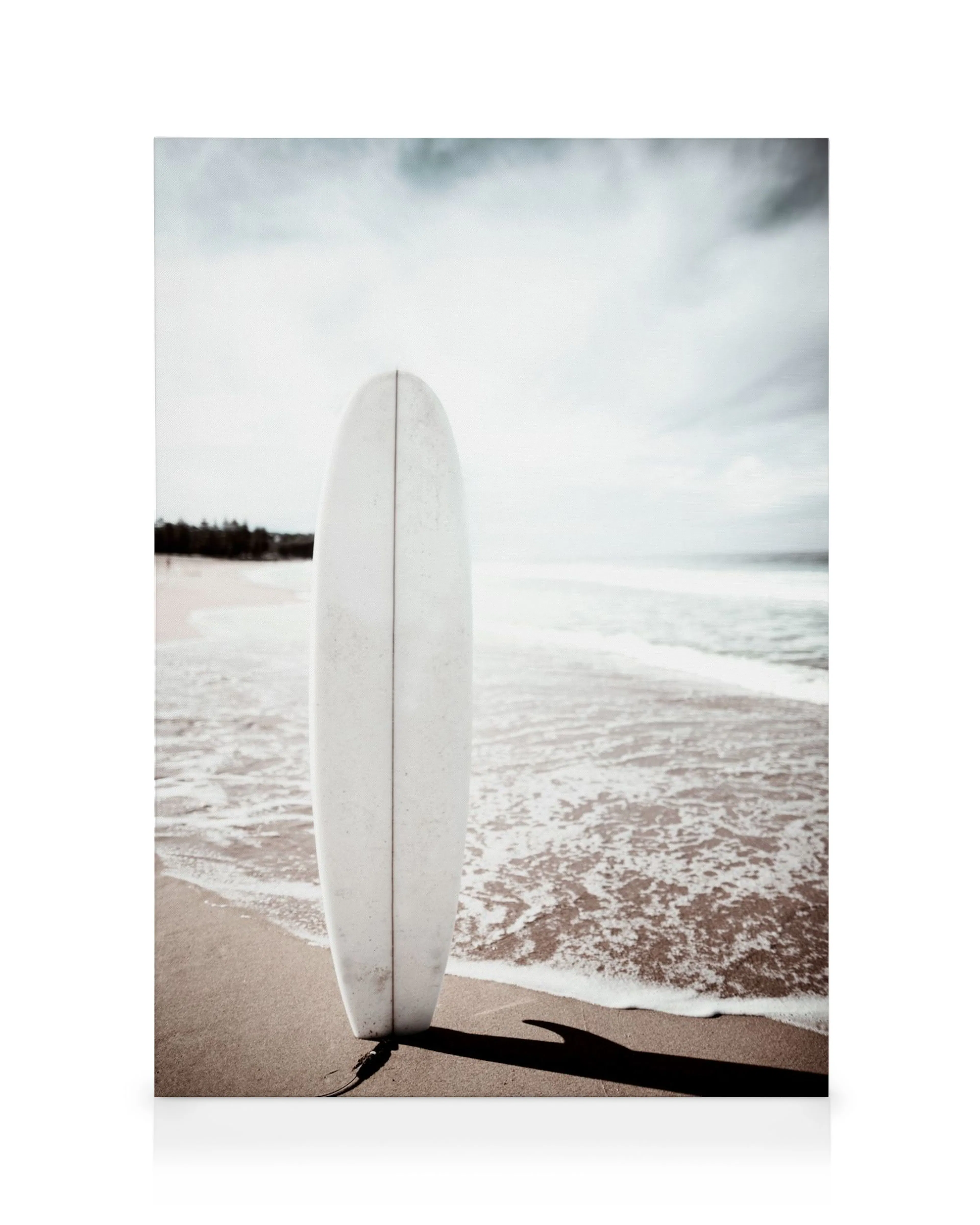 Tabla de surf blanca en playa de arena con espuma de mar y sombra, bajo cielo nublado. Arte mural costero.