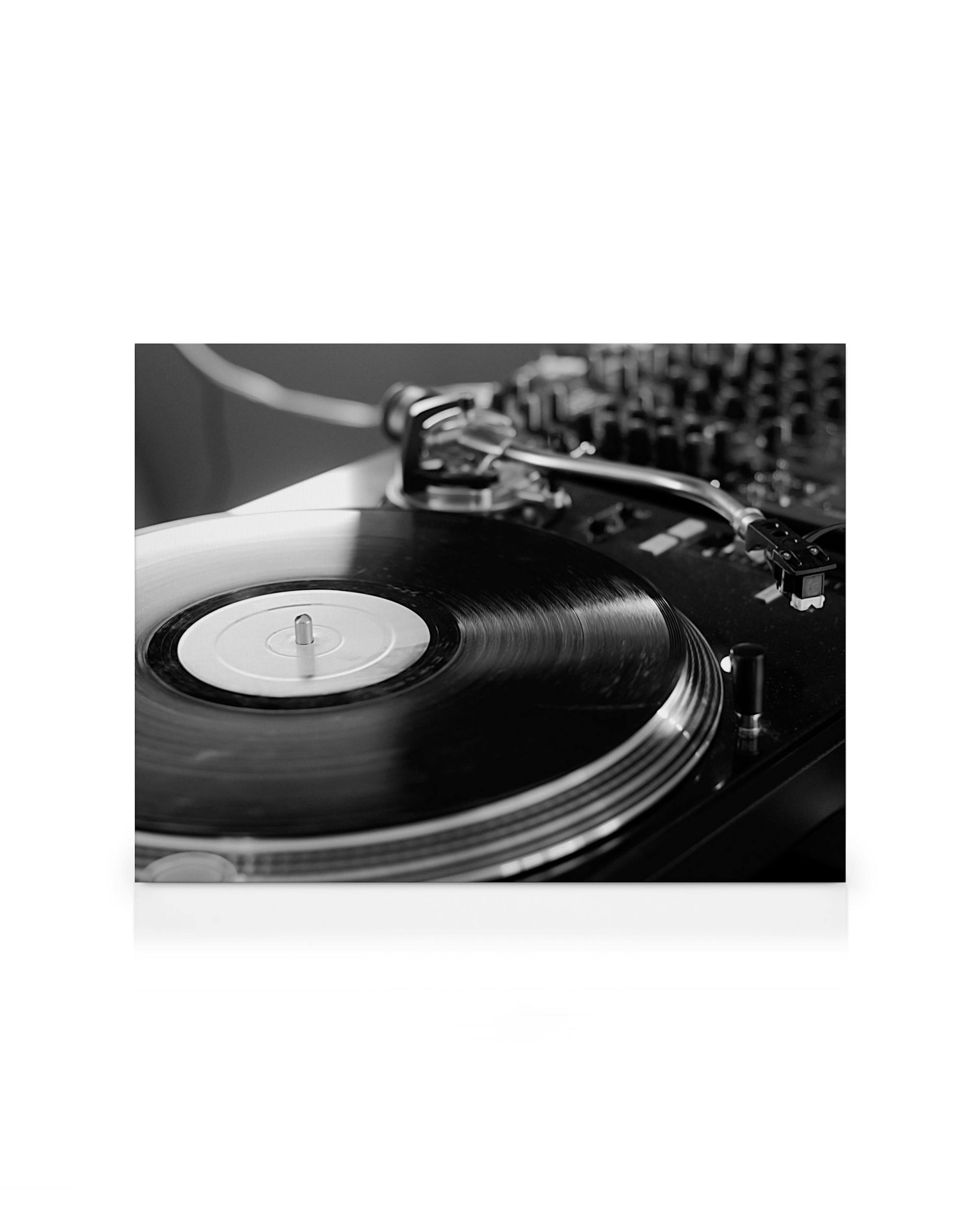 Black and white canvas print of a vinyl record on a turntable with a DJ mixer in the background, perfect for music lovers.