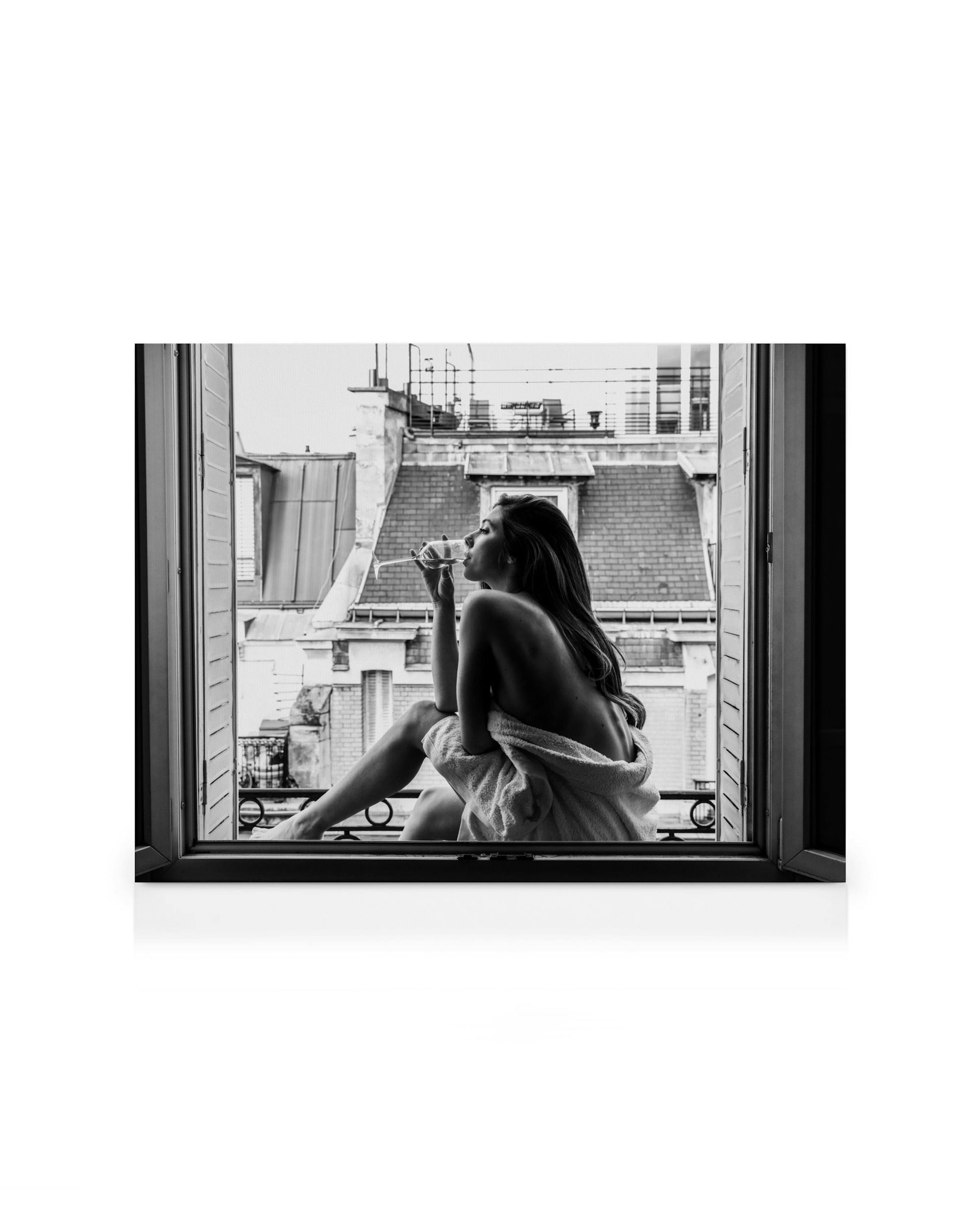 Schwarz-Weiß-Leinwandbild einer Frau im Bademantel, die aus dem Fenster blickt und Wein trinkt, mit Stadtansicht.