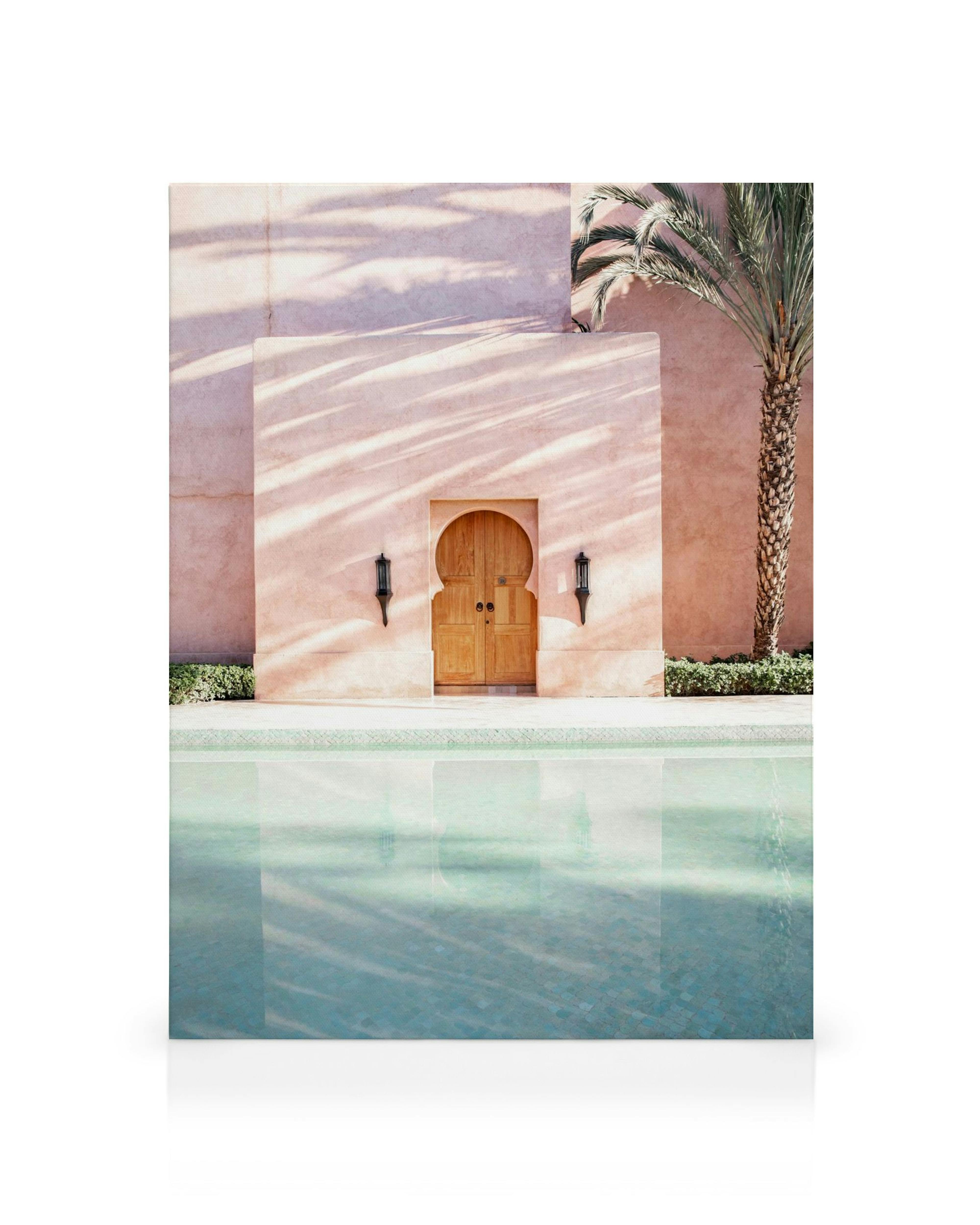 Pastellrosa marokkanische Tür mit Holztüren und Laternen, daneben ein Pool mit Palmenschatten