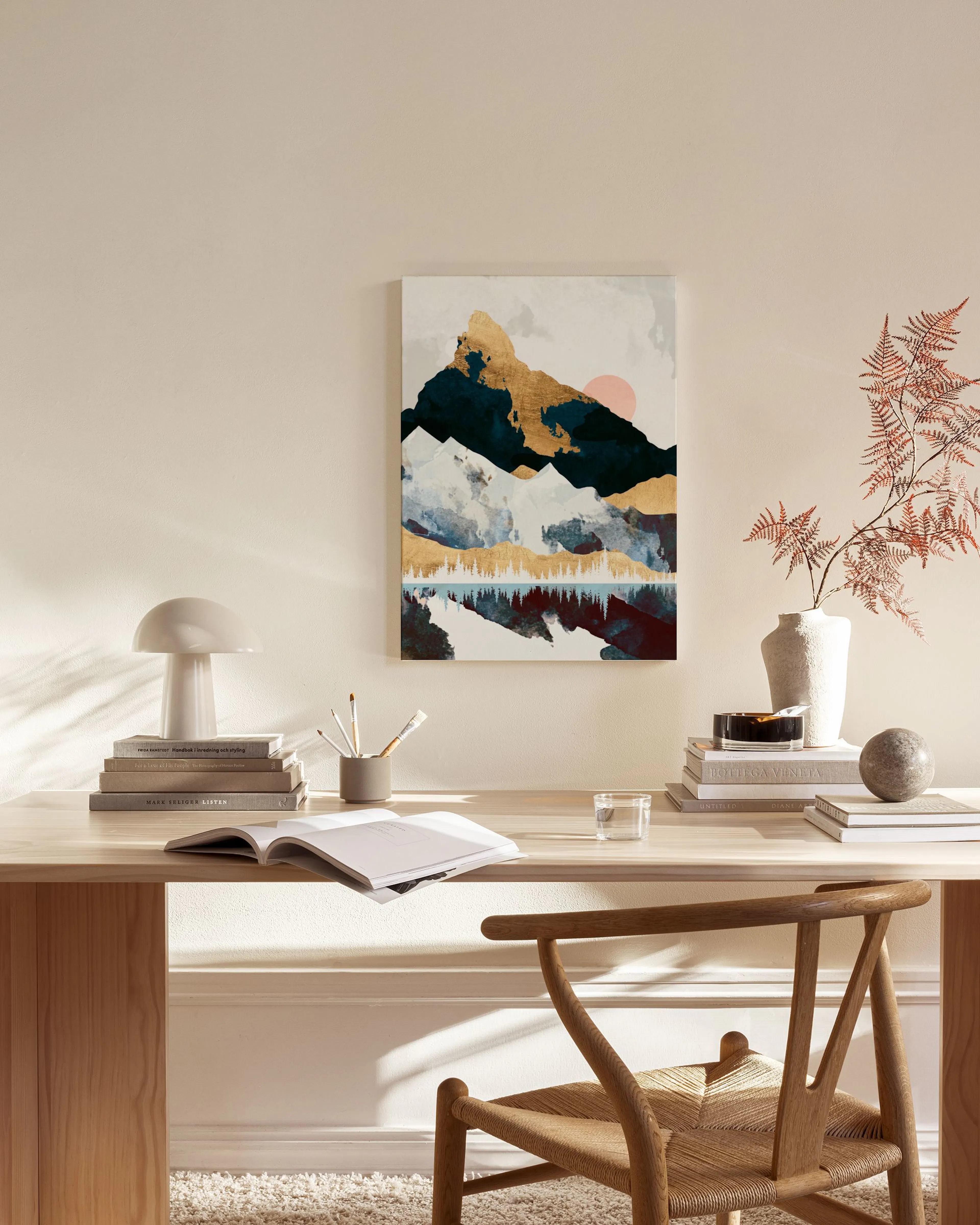 Tela decorativa com montanhas douradas, azuis e brancas sobre um lago, com um sol rosa, numa sala de estar moderna.