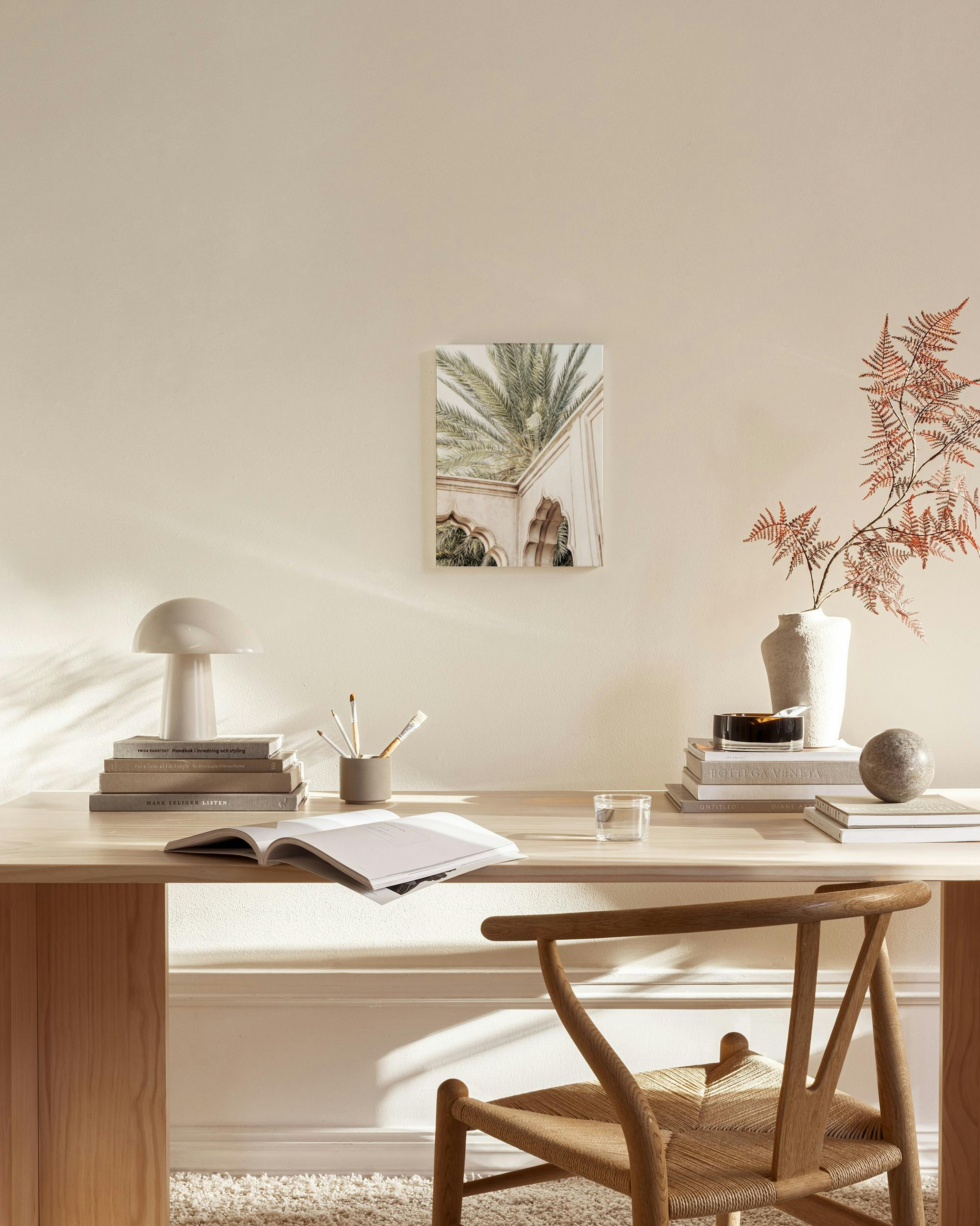 A canvas print of palm fronds and archways from a building, hanging above a wooden console table in a minimalist living room.