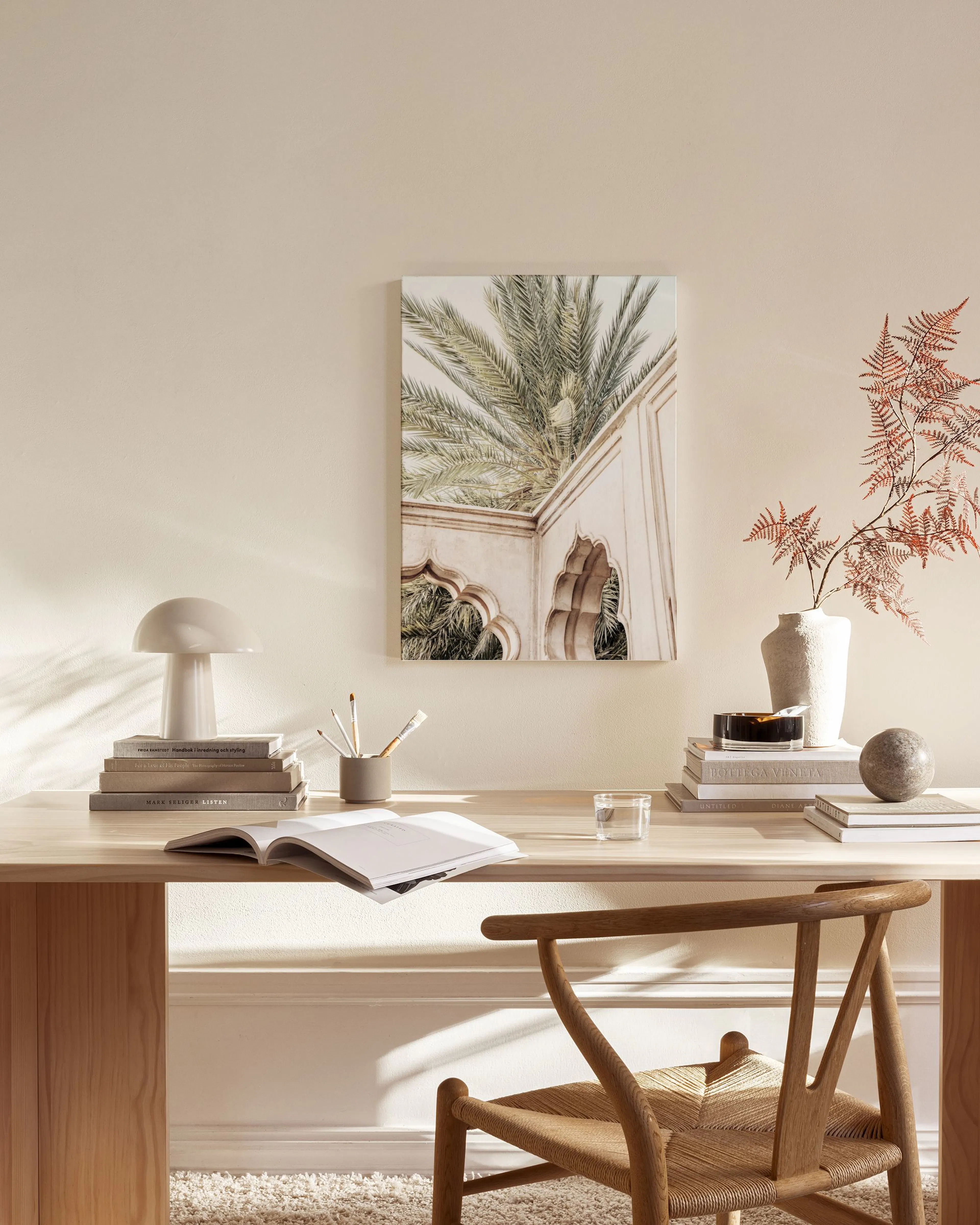 Lienzo con palmeras y arquitectura árabe, colgado en una sala de estar moderna con mesa de centro y butaca de madera.