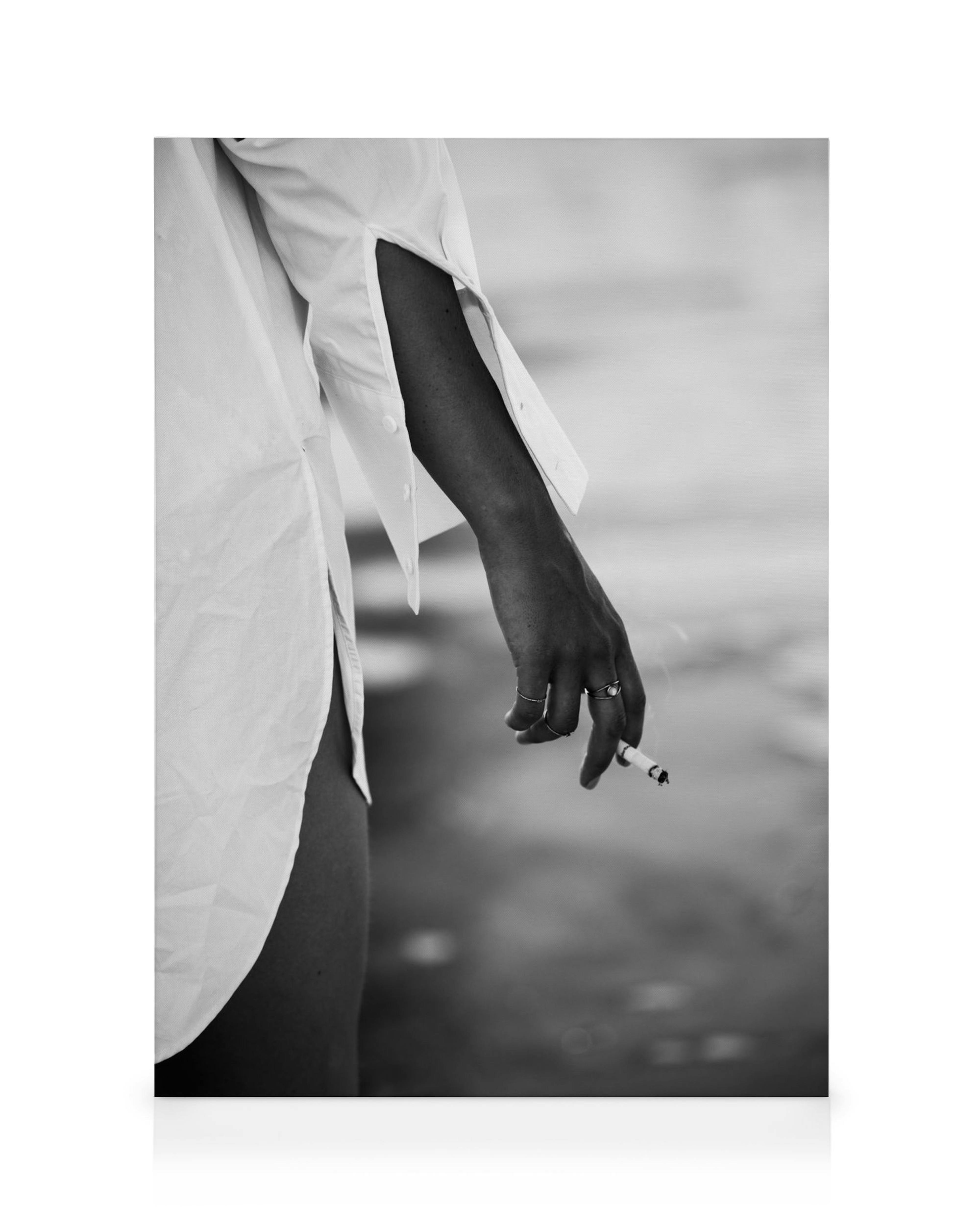 Black and white photography of a girl in a white shirt holding a cigarette, with rings on her fingers, exuding a moody atmospher