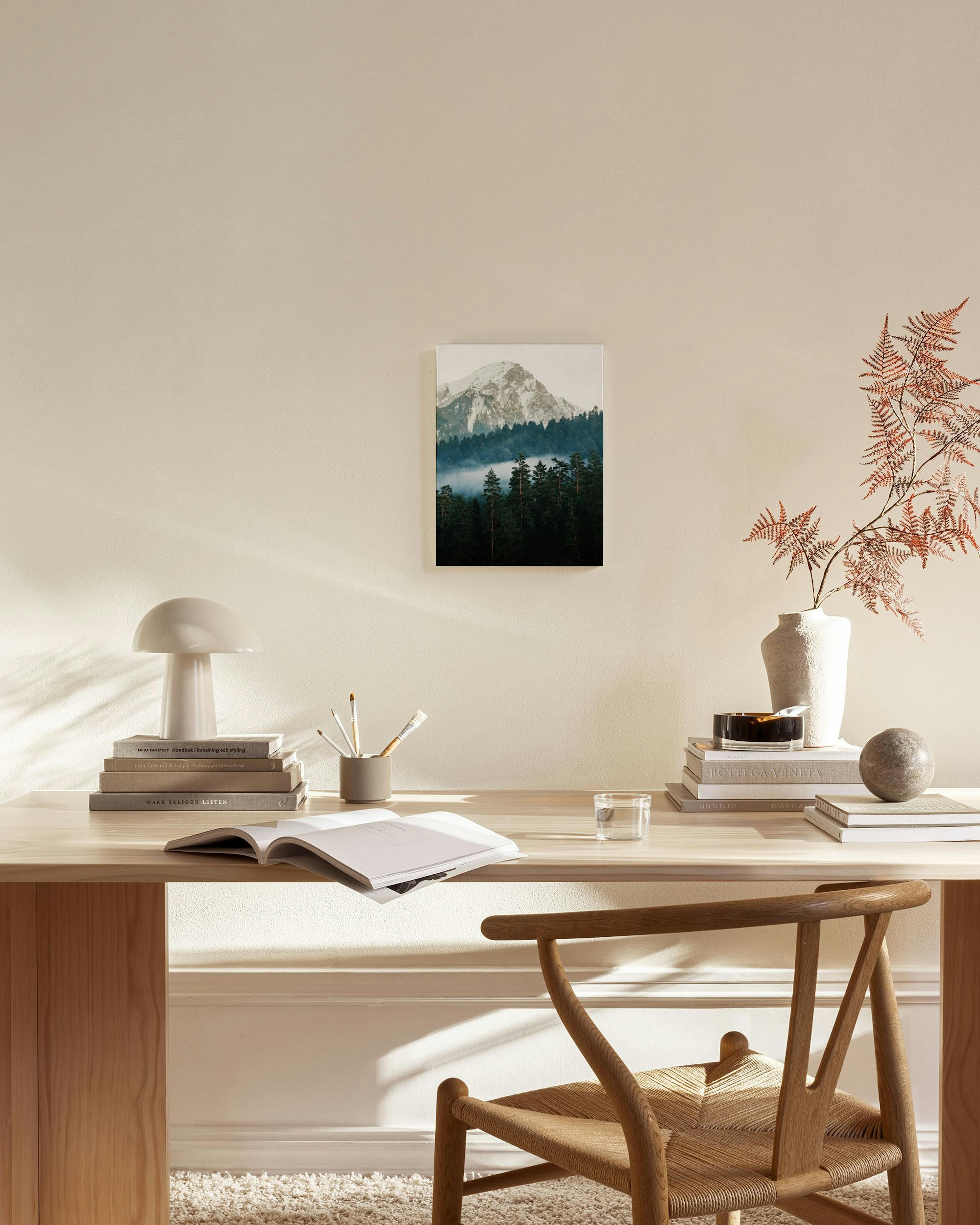 A canvas print of a snow-capped mountain above a forest with misty pines, displayed in a bright living room.