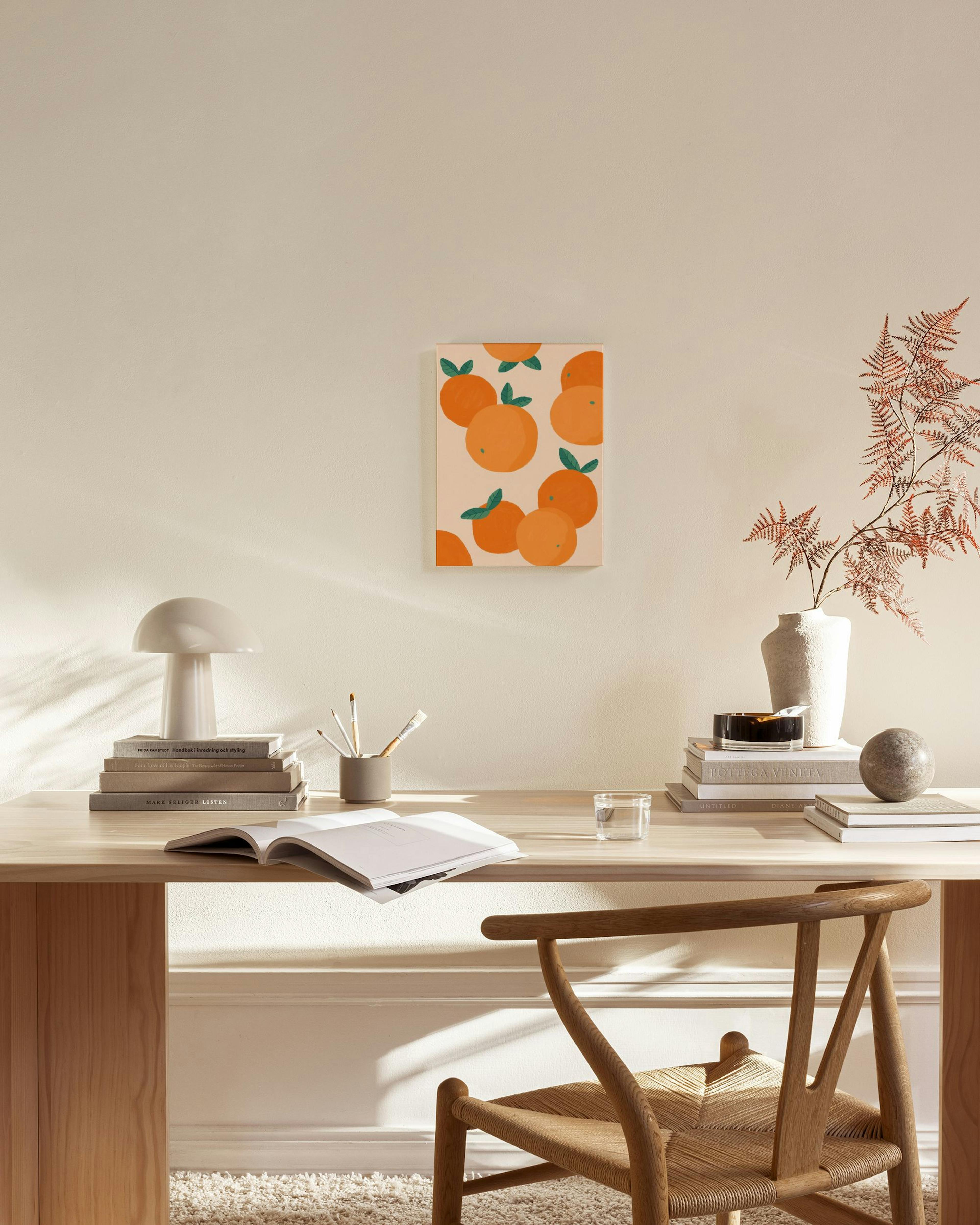 A canvas print of scattered oranges with green leaves on a light background, hanging in a bright, modern living room.