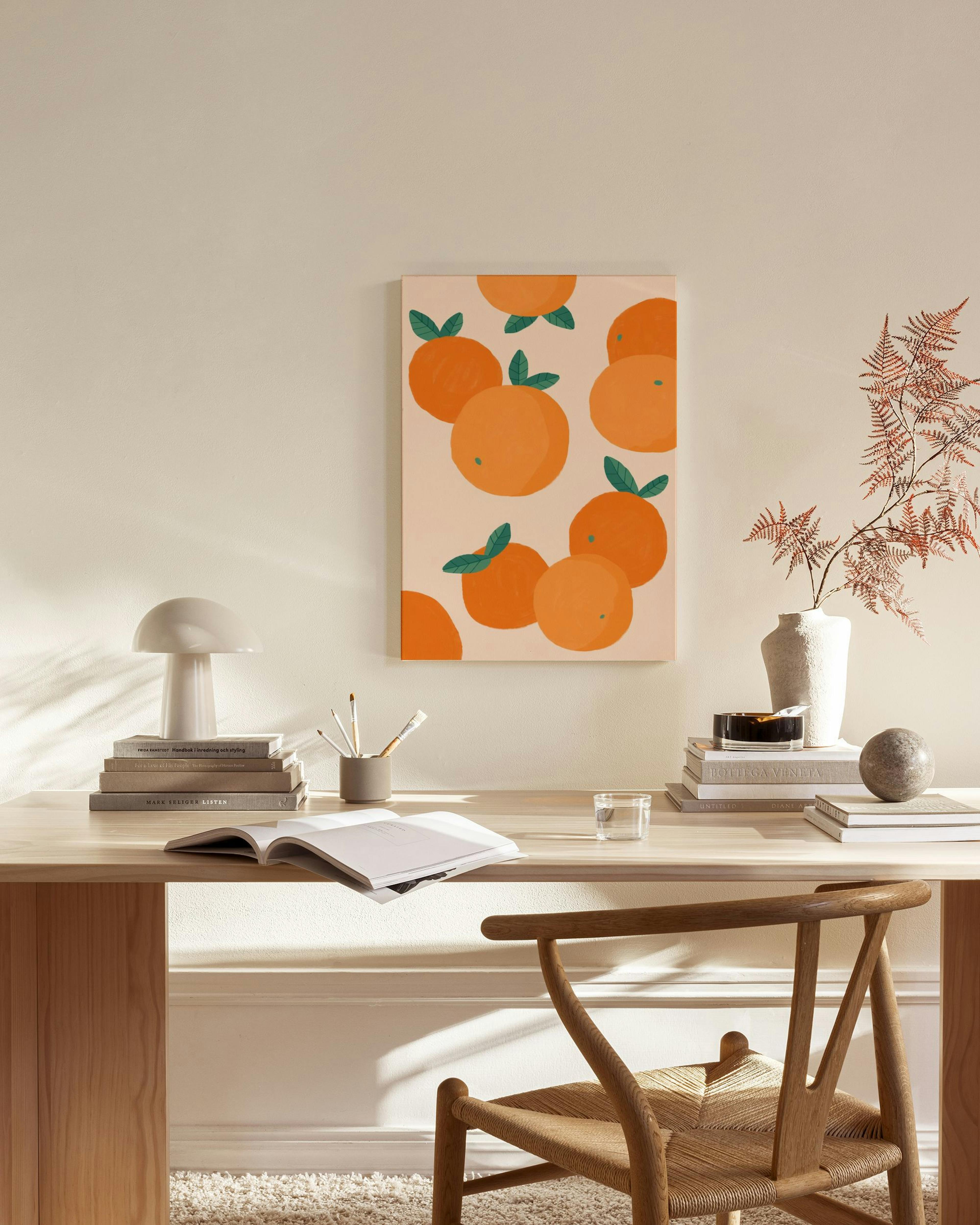 Canvas met oranje sinaasappels en groene bladeren op roze achtergrond, hangend in een moderne, lichte woonkamer.