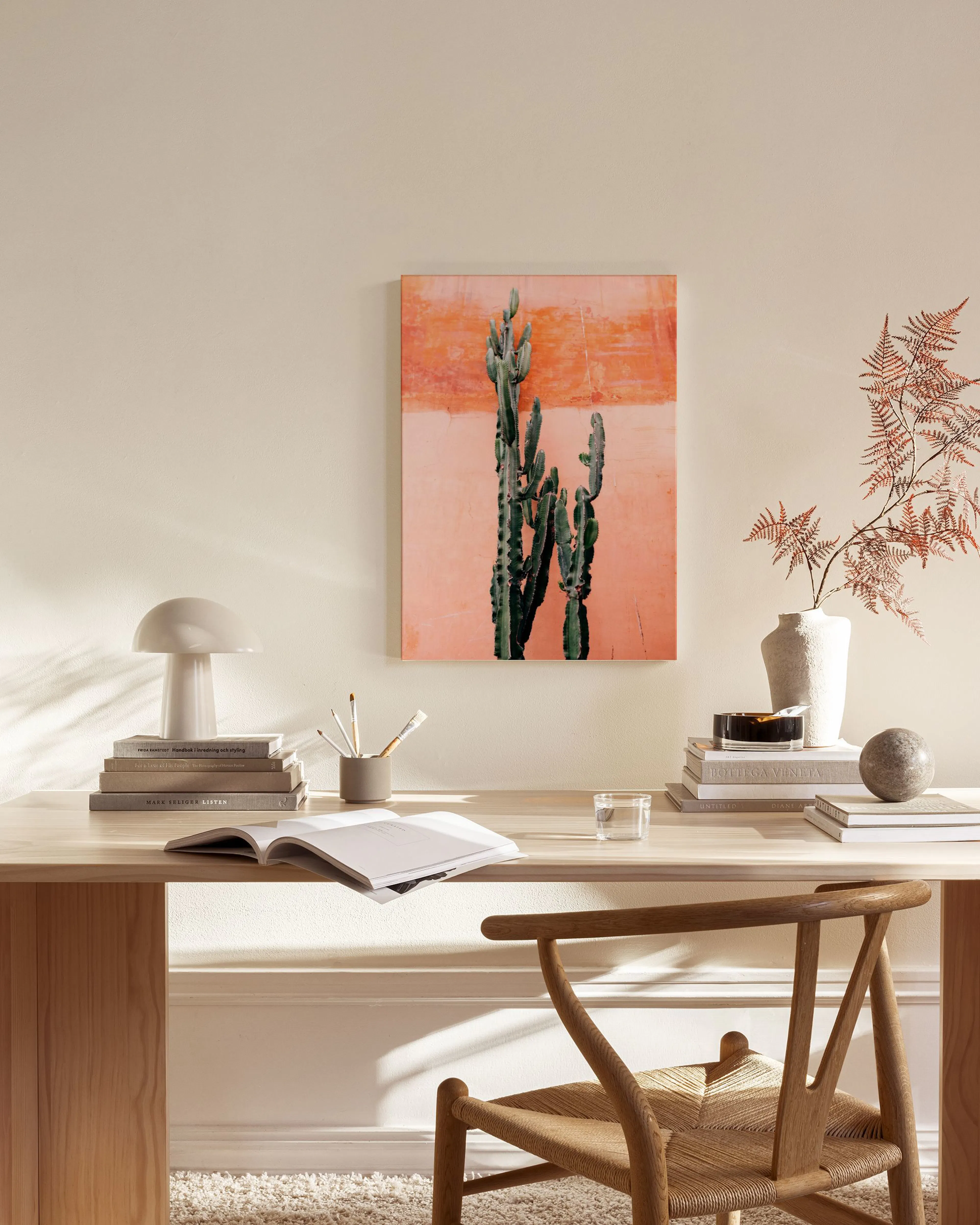 A desert cactus print with a textured peach background, hanging above a wooden console table in a living room.