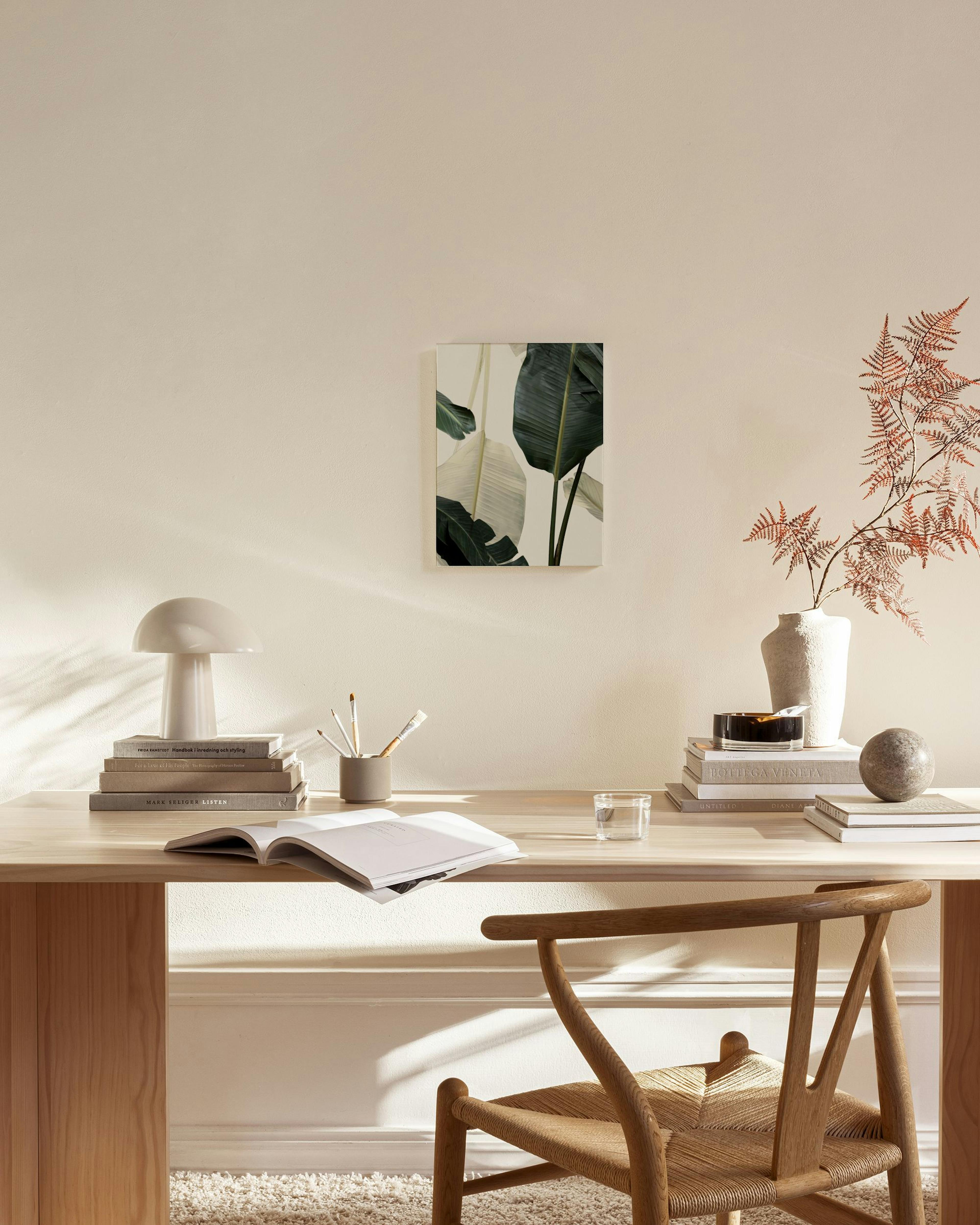 A canvas print of large, dark green and pale green tropical leaves, hanging in a bright, minimalist living room.