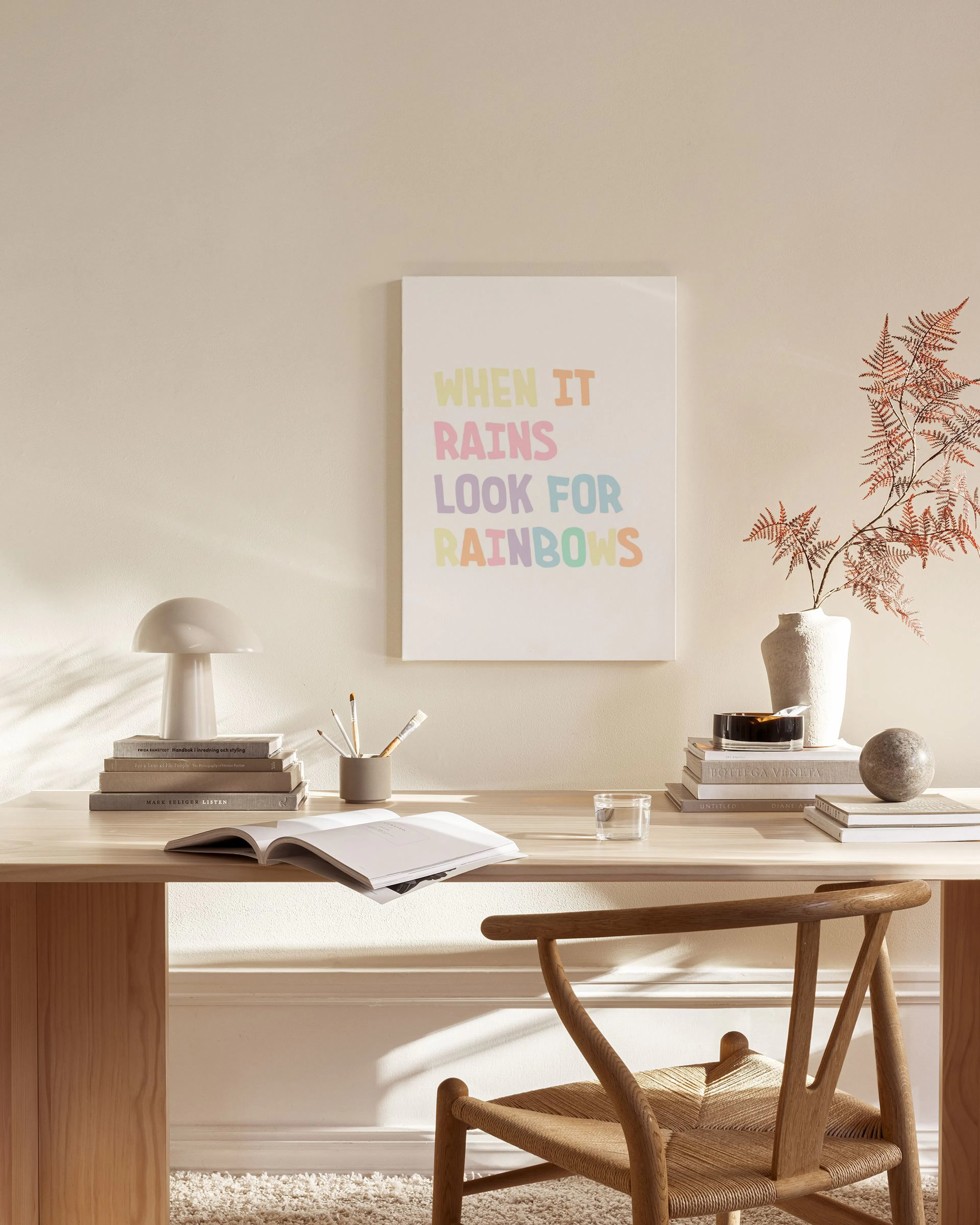 Toile murale avec l’inscription colorée WHEN IT RAINS LOOK FOR RAINBOWS sur fond blanc, dans un salon moderne.