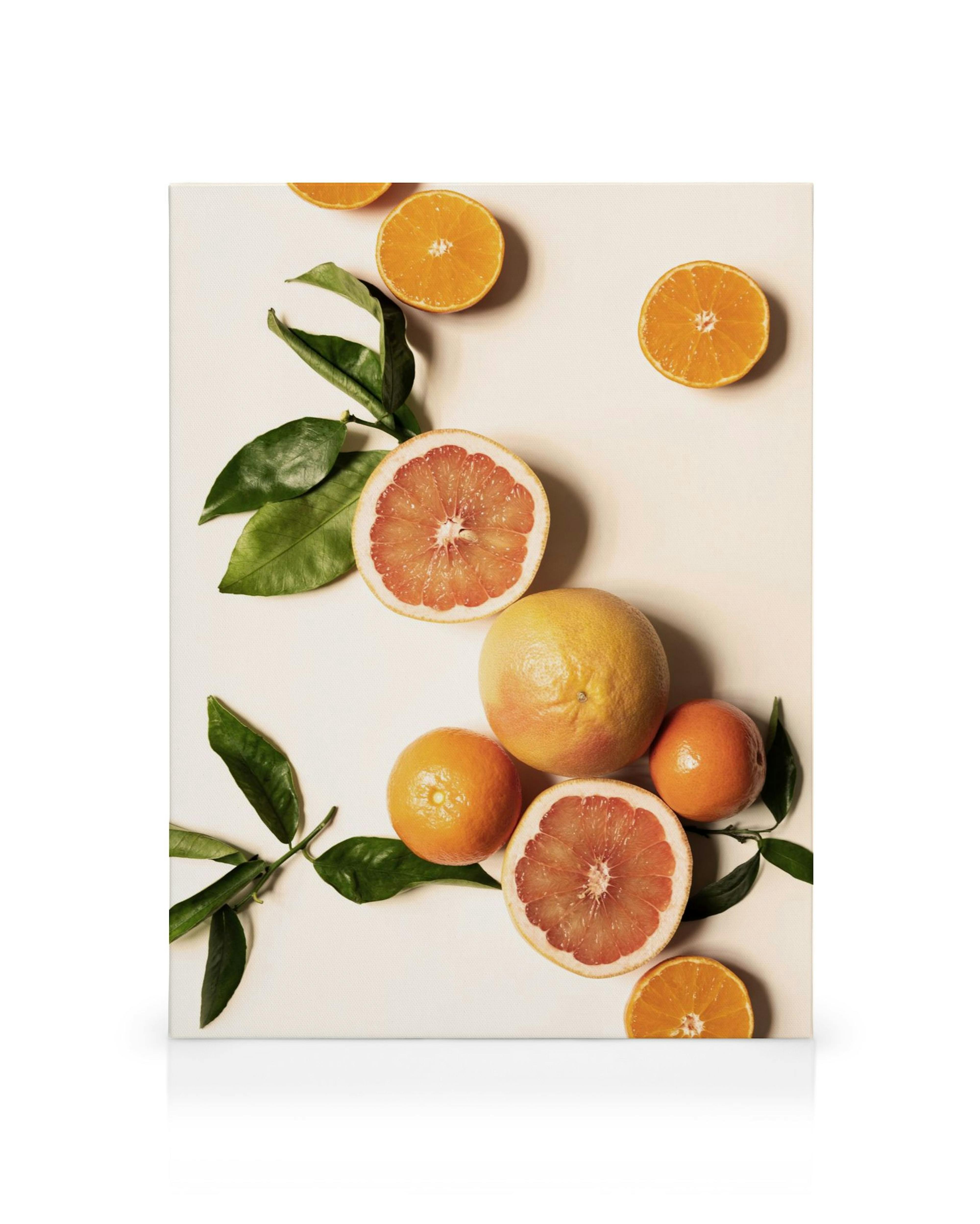 Vibrant canvas print of oranges and grapefruit with green leaves on a white surface, perfect for kitchen decor.