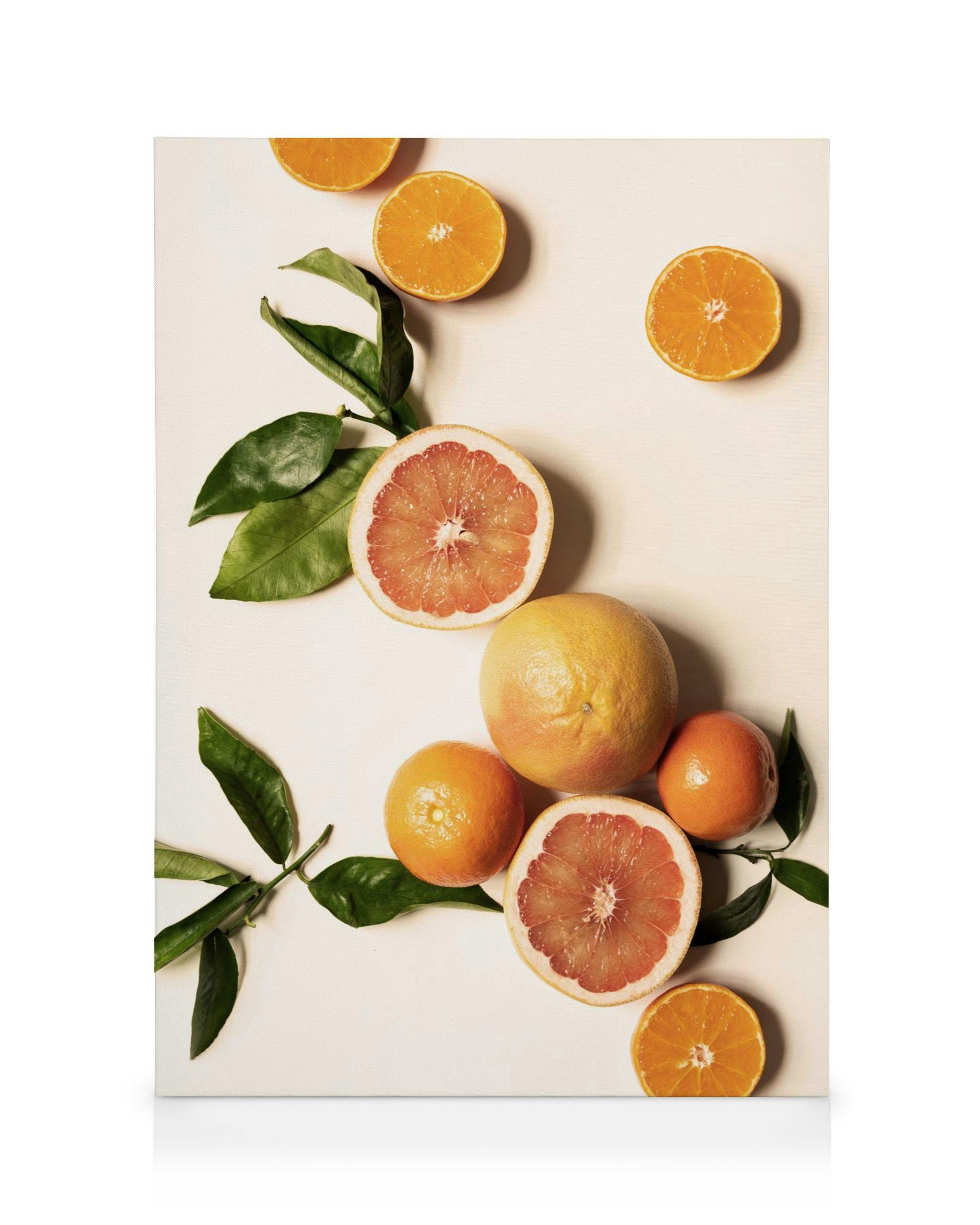 Leinwandbild mit frischen, aufgeschnittenen Zitrusfrüchten, Grapefruits und Orangen, dazu grüne Blätter auf hellem Hintergrund.
