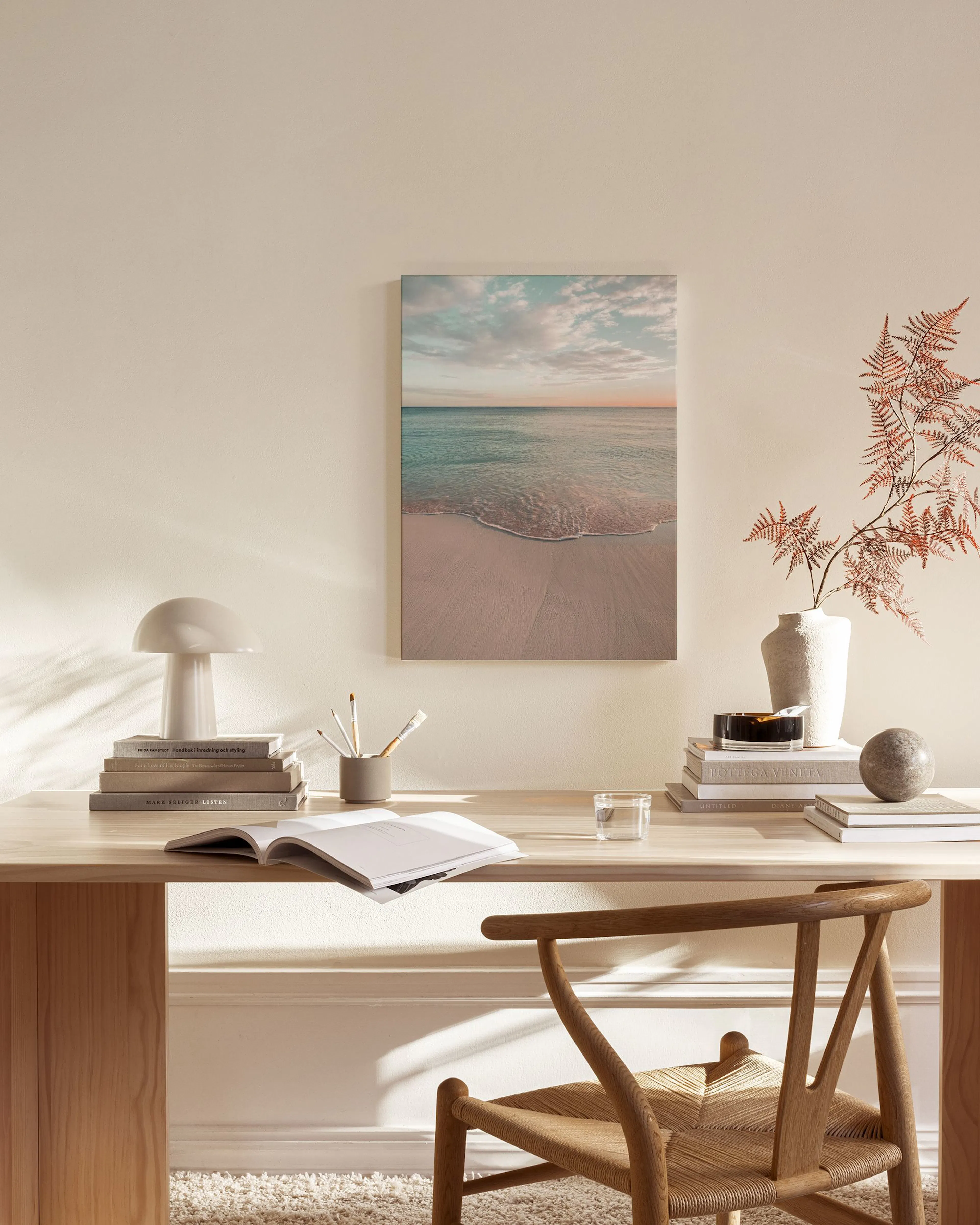 A serene beach scene with calm waves on light sand under a pastel sky, hanging in a modern living room.