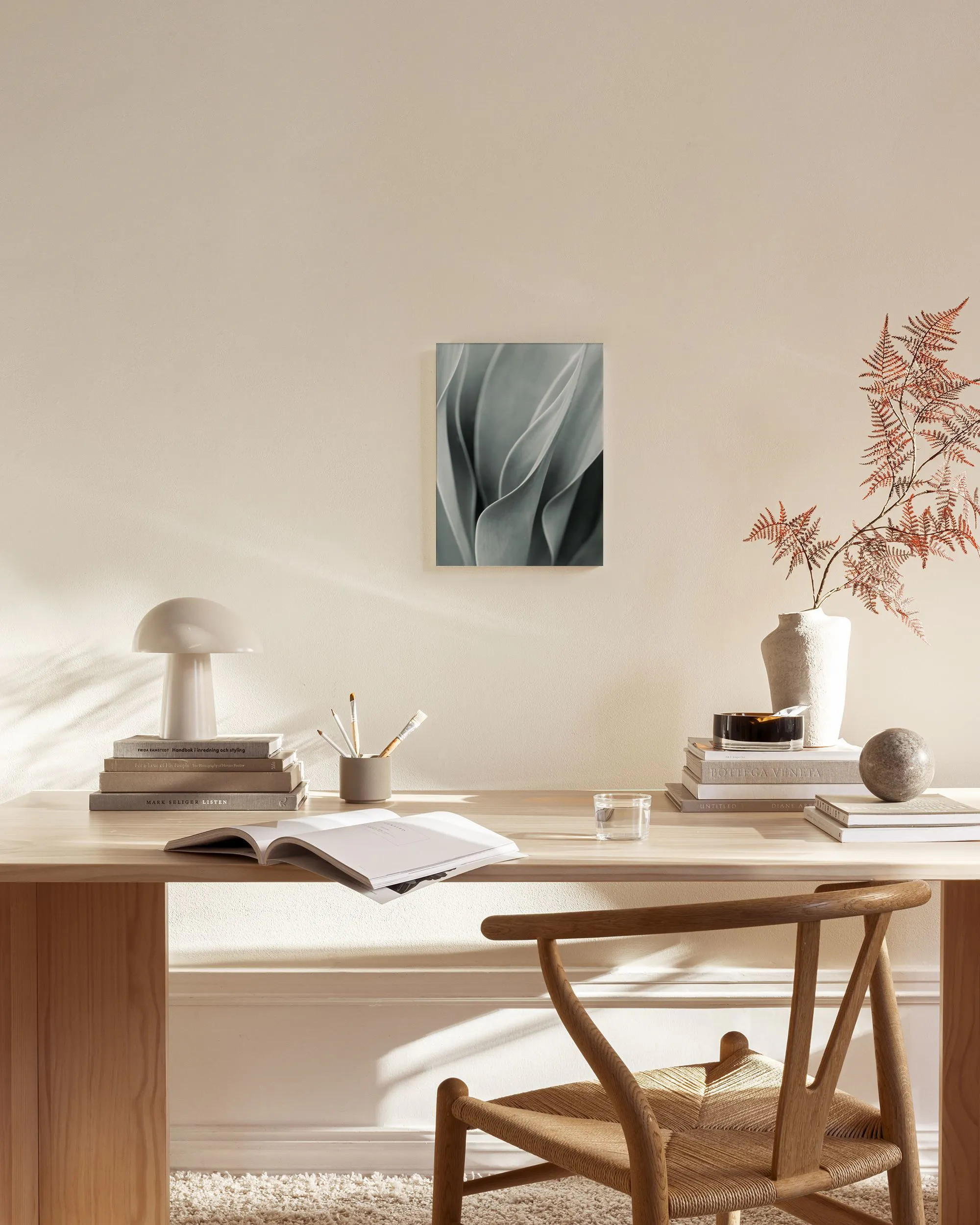 Toile murale de feuilles de plante succulente gris-vert, dans un salon lumineux avec un fauteuil en bois et une table basse.