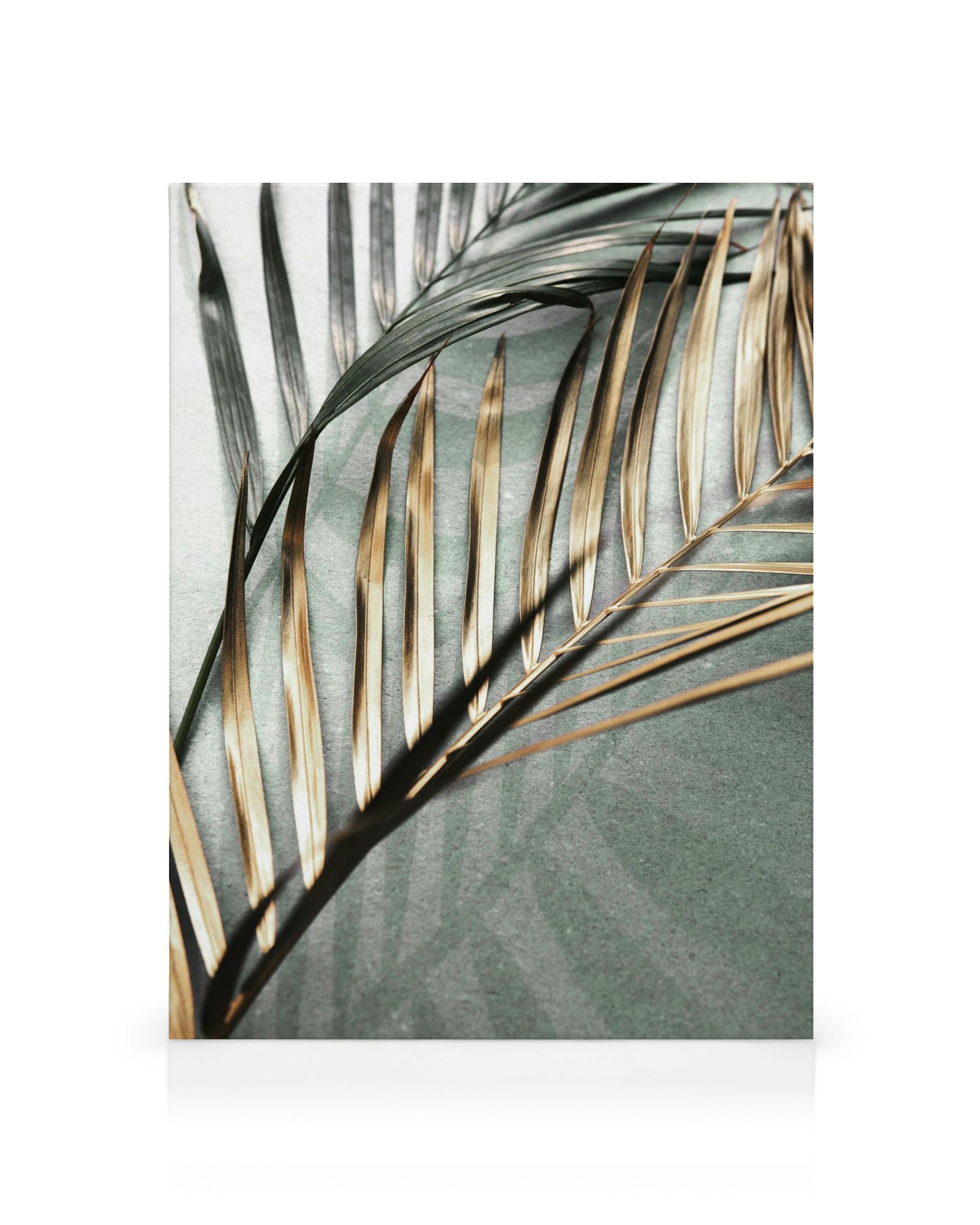 Canvastavla med skimrande guld- och mörkgröna palmblad som kastar skuggor mot en grågrön bakgrund, naturinspirerad konst.