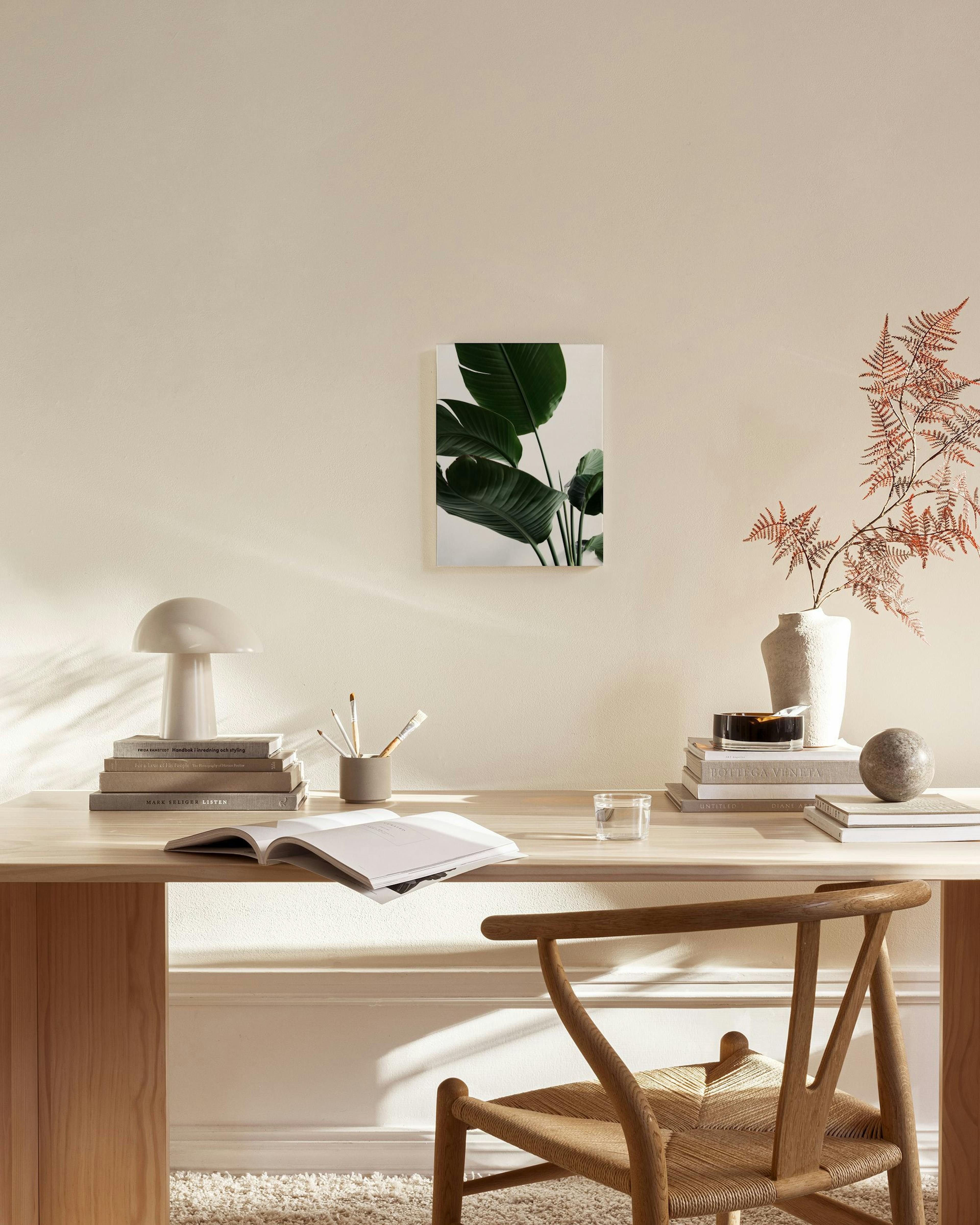 Stampa su tela con foglie verdi di pianta tropicale, appesa in un salotto moderno sopra una credenza in legno.