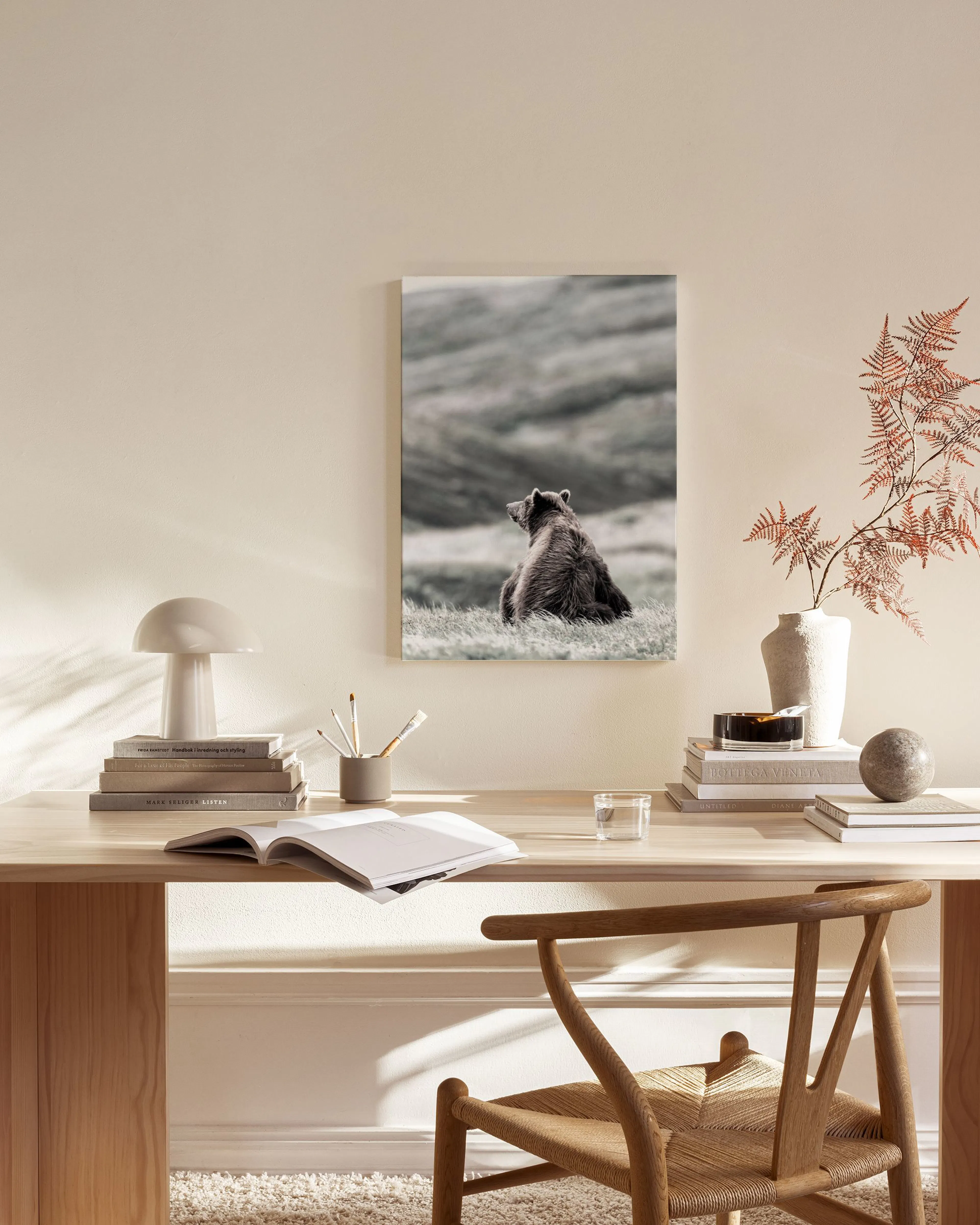 A canvas print of a brown bear sitting in a grassy landscape, hanging in a light-toned living room above a wooden console table.