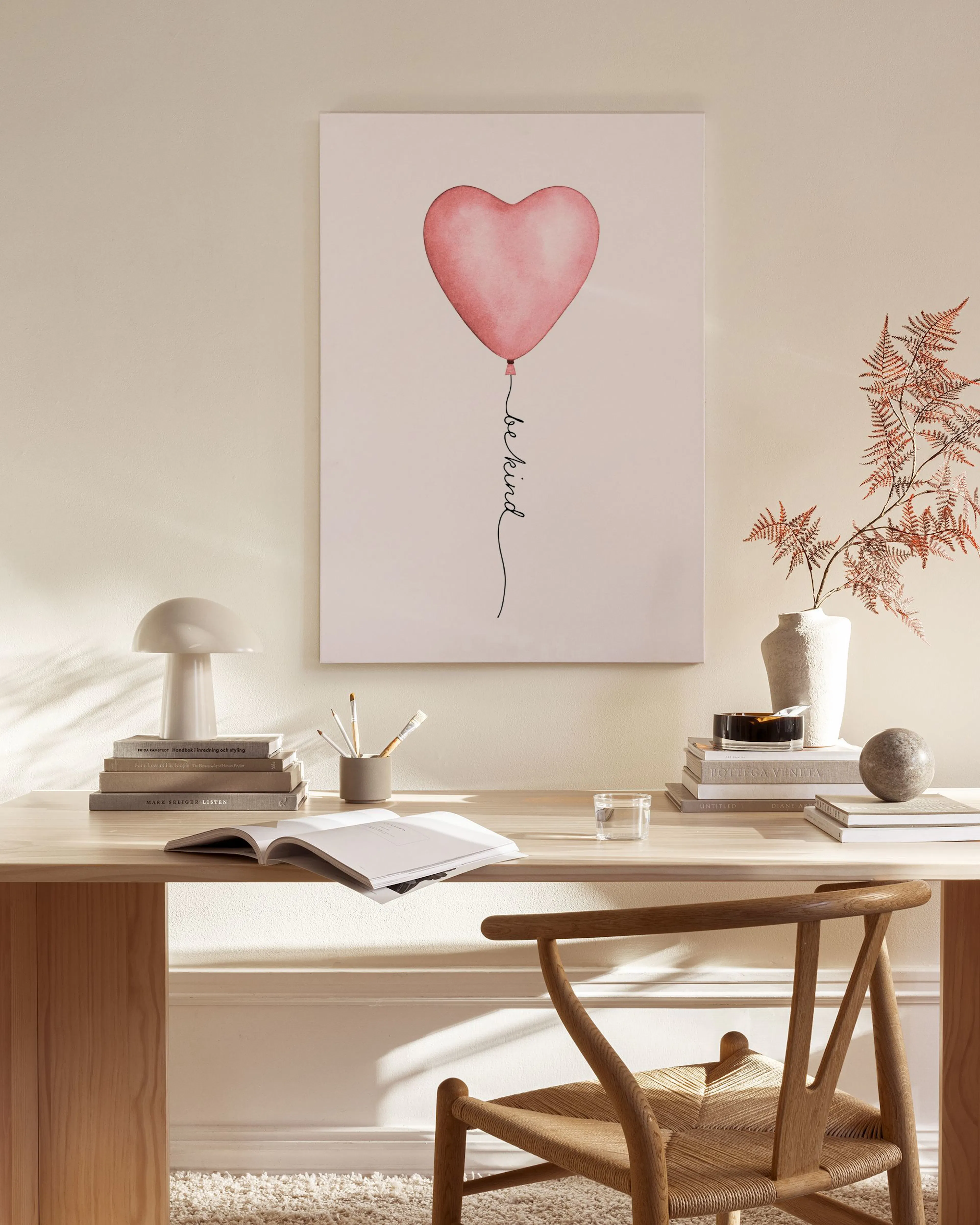 A canvas print of a pink heart balloon with be kind written on its string, hanging in a bright, modern living room.