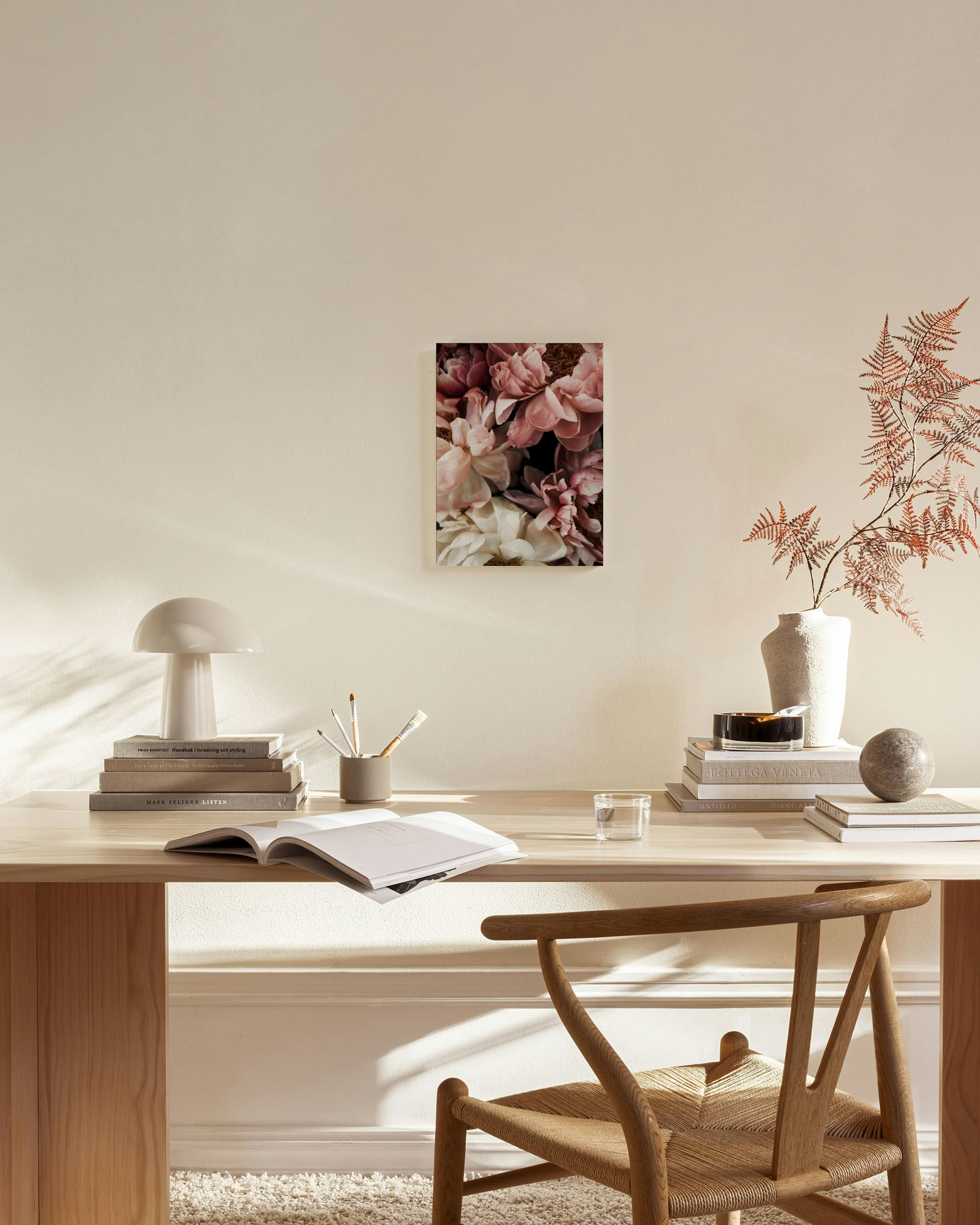 A canvas print of pink and white peony flowers hanging on a light beige wall above a wooden console table in a living room.