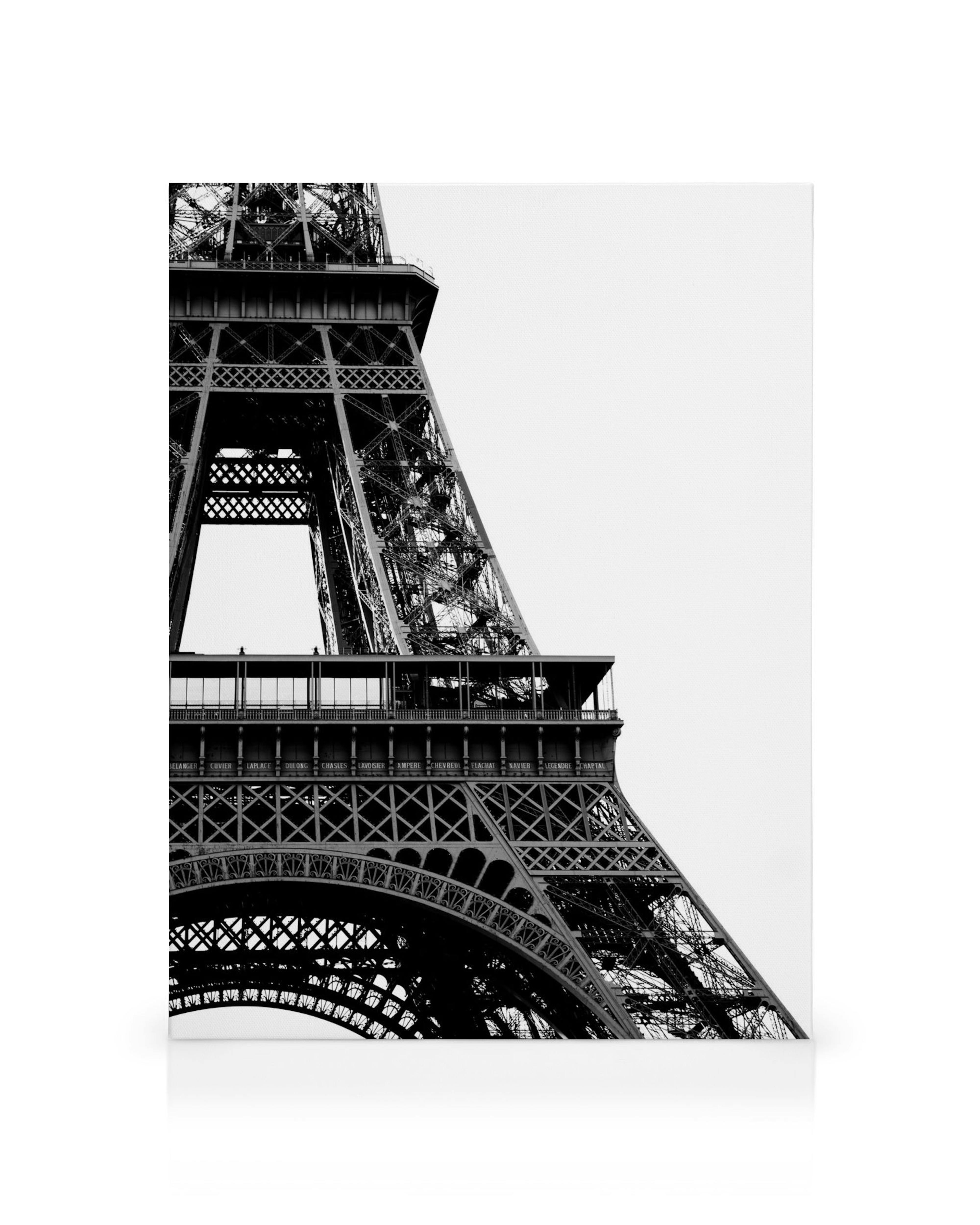 Close-up black and white photo of the Eiffel Tower, showcasing its intricate ironwork against a light sky.