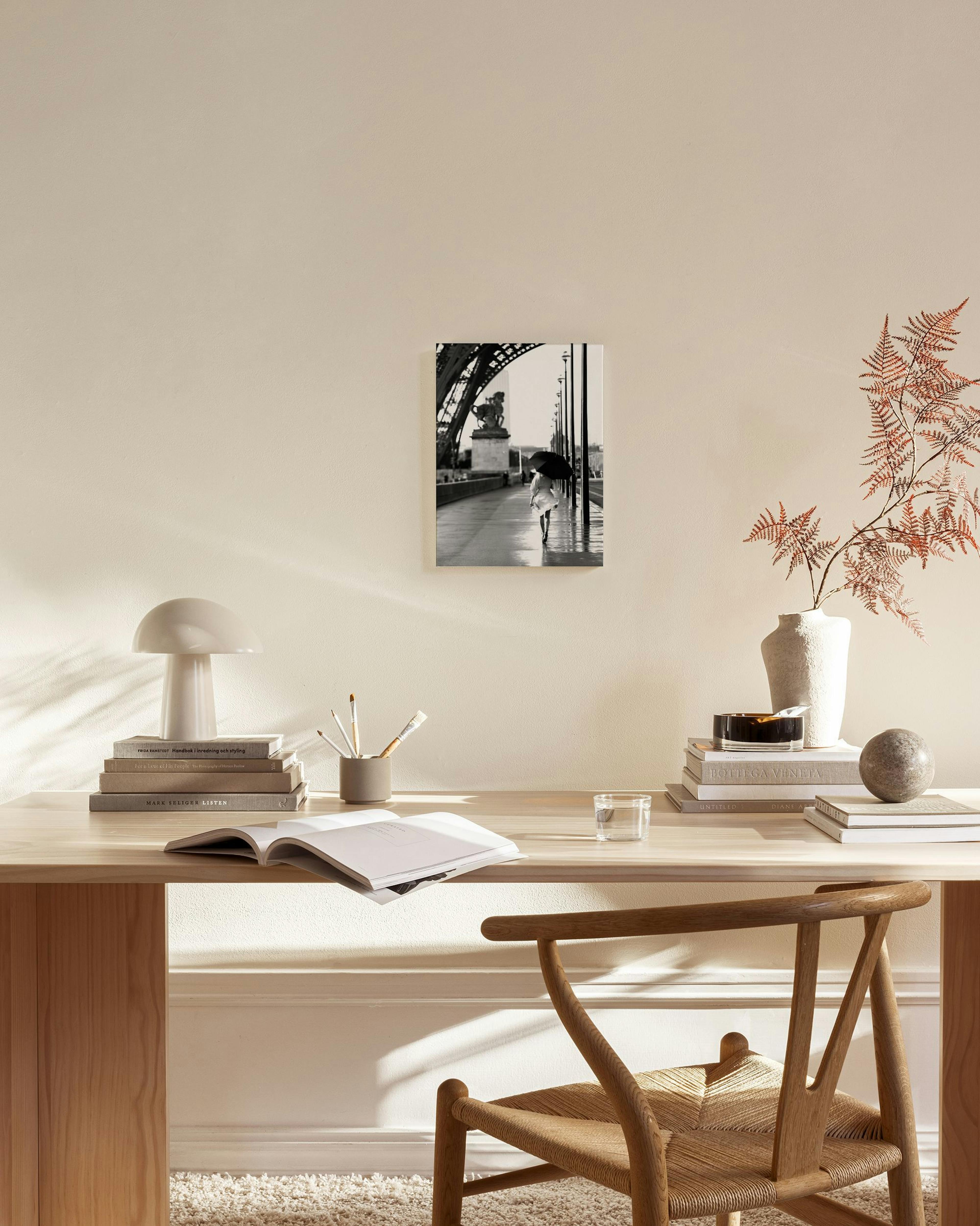 Zwart-wit canvas van een persoon met paraplu op een natte brug, hangend boven een houten dressoir in een lichte woonkamer.