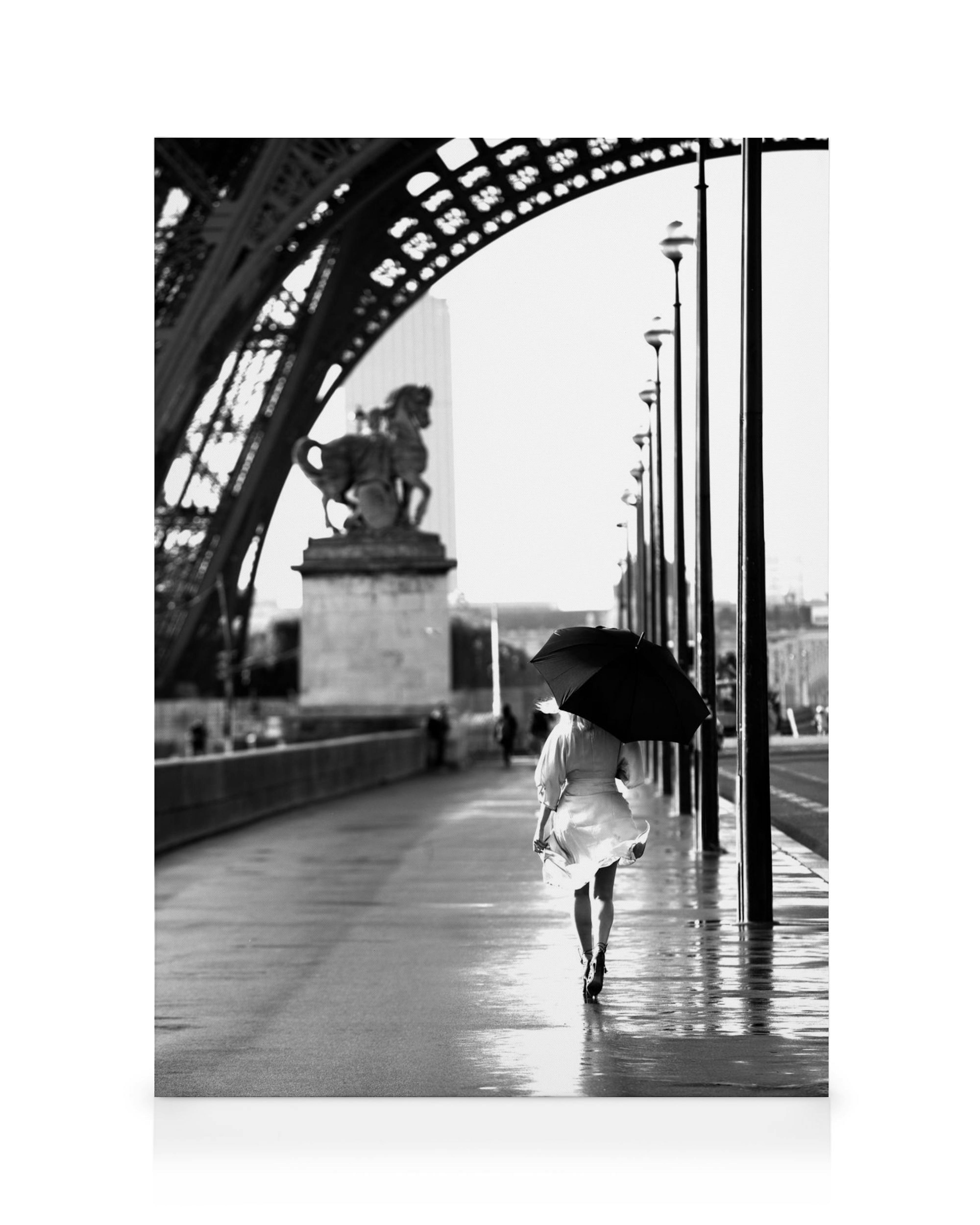 Mulher com guarda-chuva preto caminhando em Paris, rua molhada, Ponte Alexandre III e Torre Eiffel no fundo, preto e branco