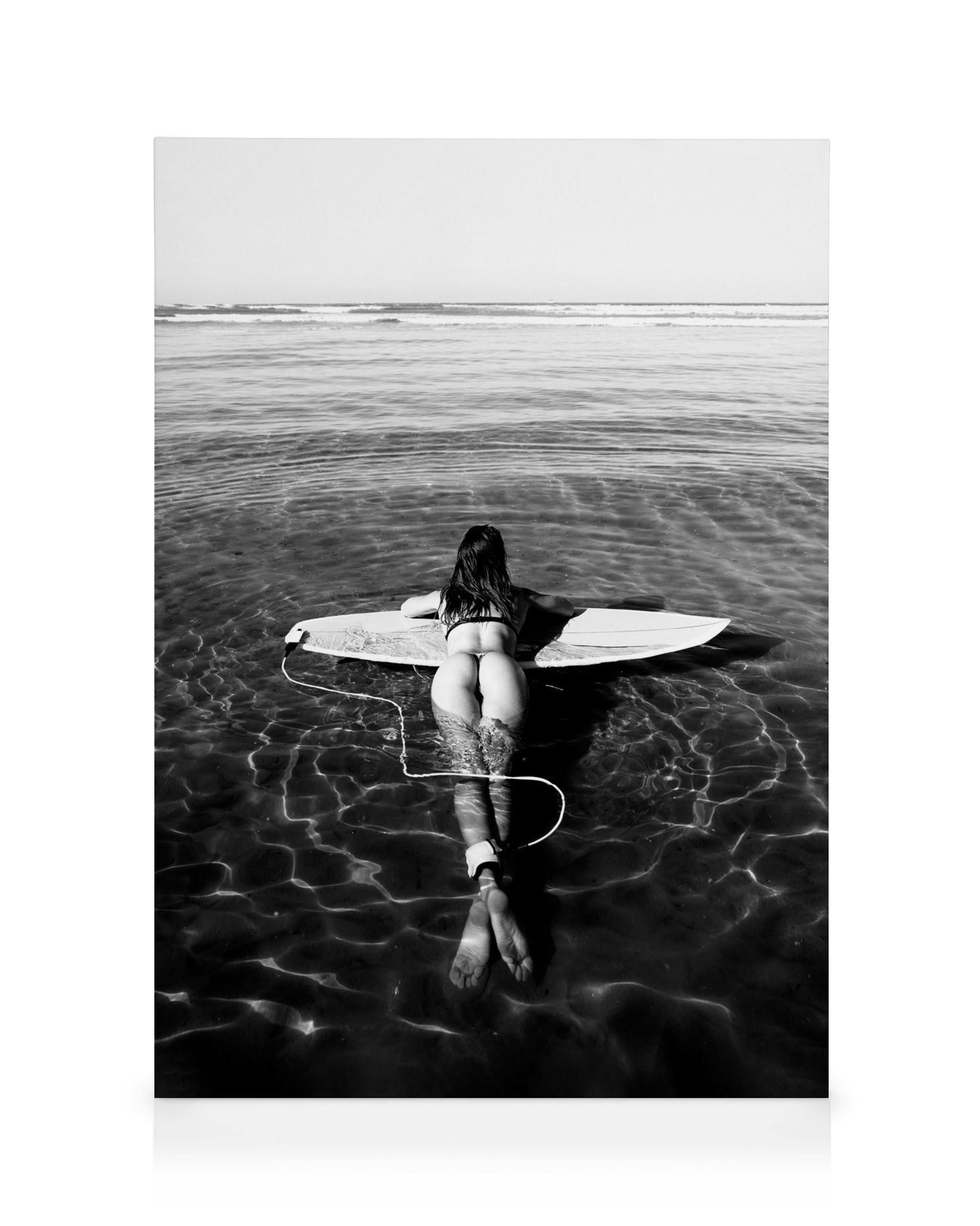 Monochromatic black and white photo of a woman in clear water, floating on a surfboard, facing away from the camera.