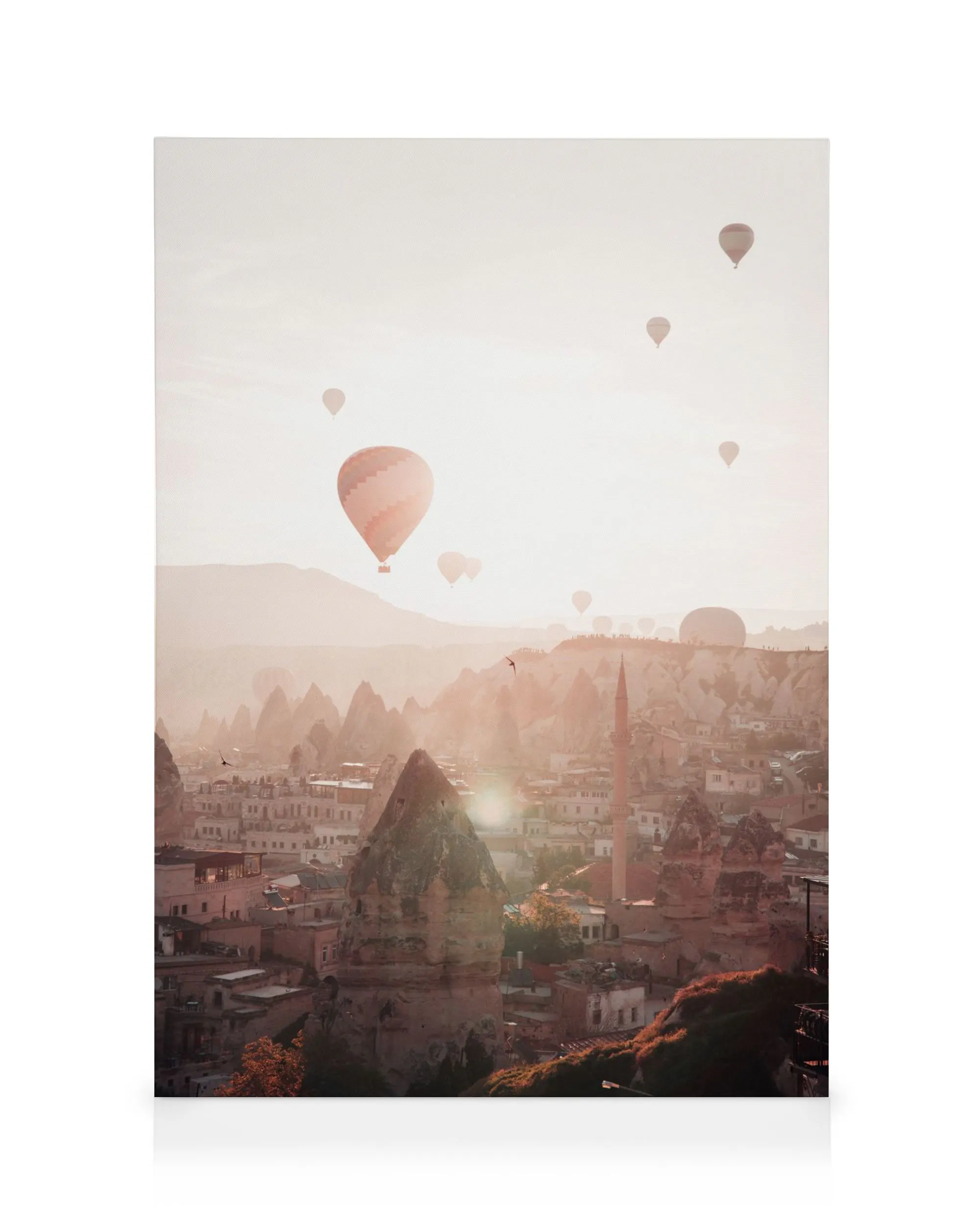 Canvastavla med luftballonger över Kappadokien vid soluppgången, rosa himmel och klippiga landskap med byggnader.