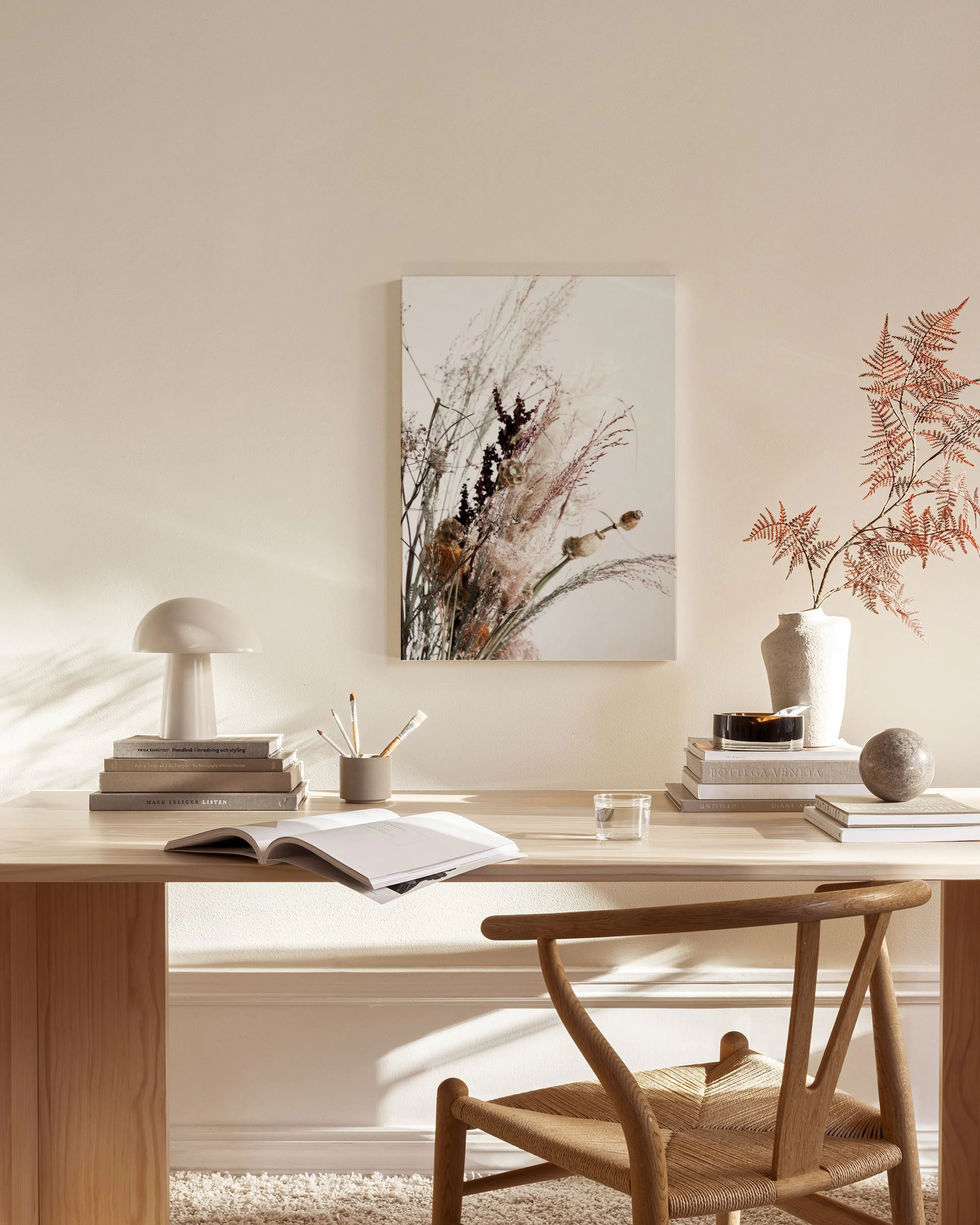A canvas print of dried floral arrangements in warm tones, hanging in a minimalist living room setting.