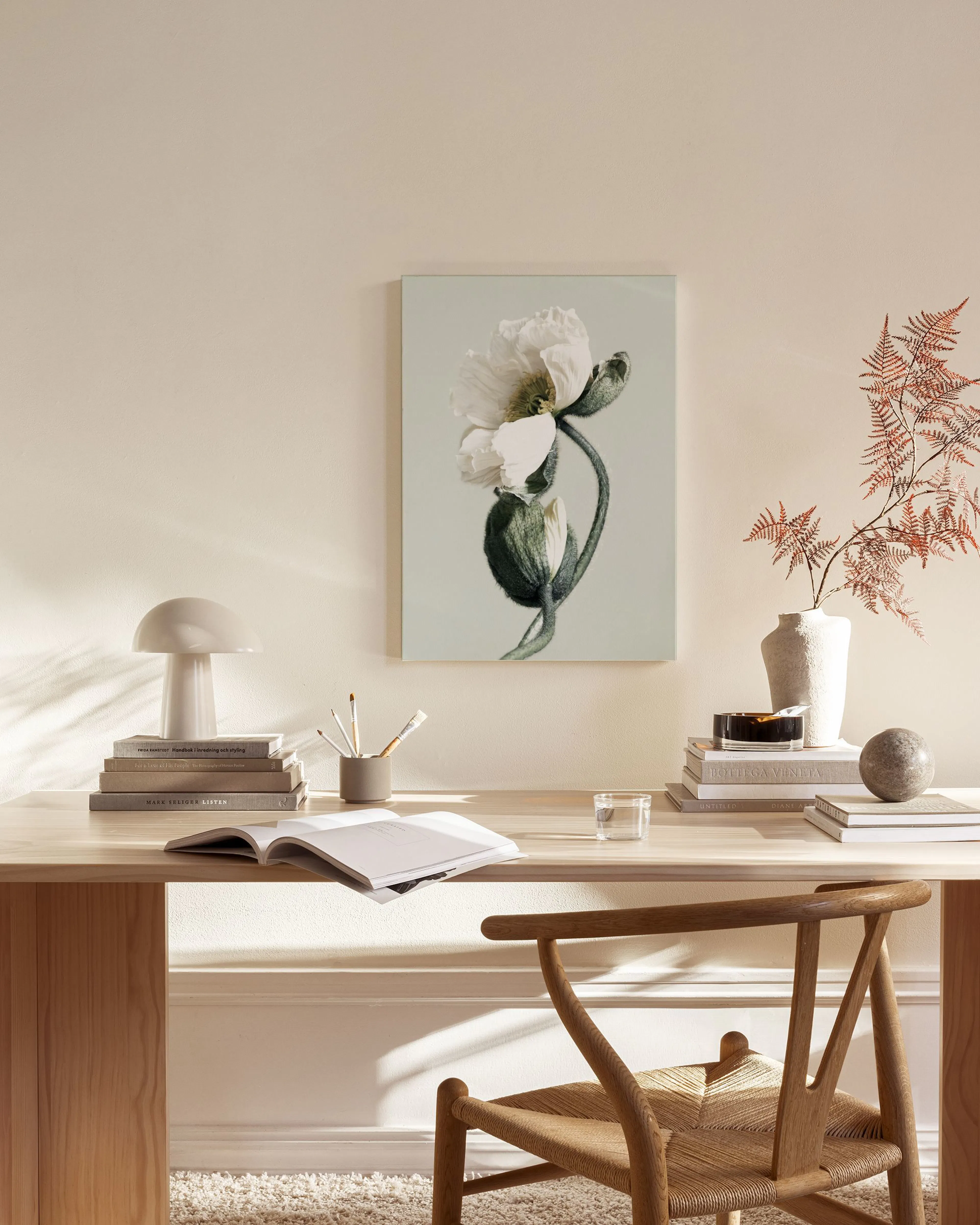 A canvas print of a white poppy flower with a closed bud on a light green background, hanging in a minimalist living room.