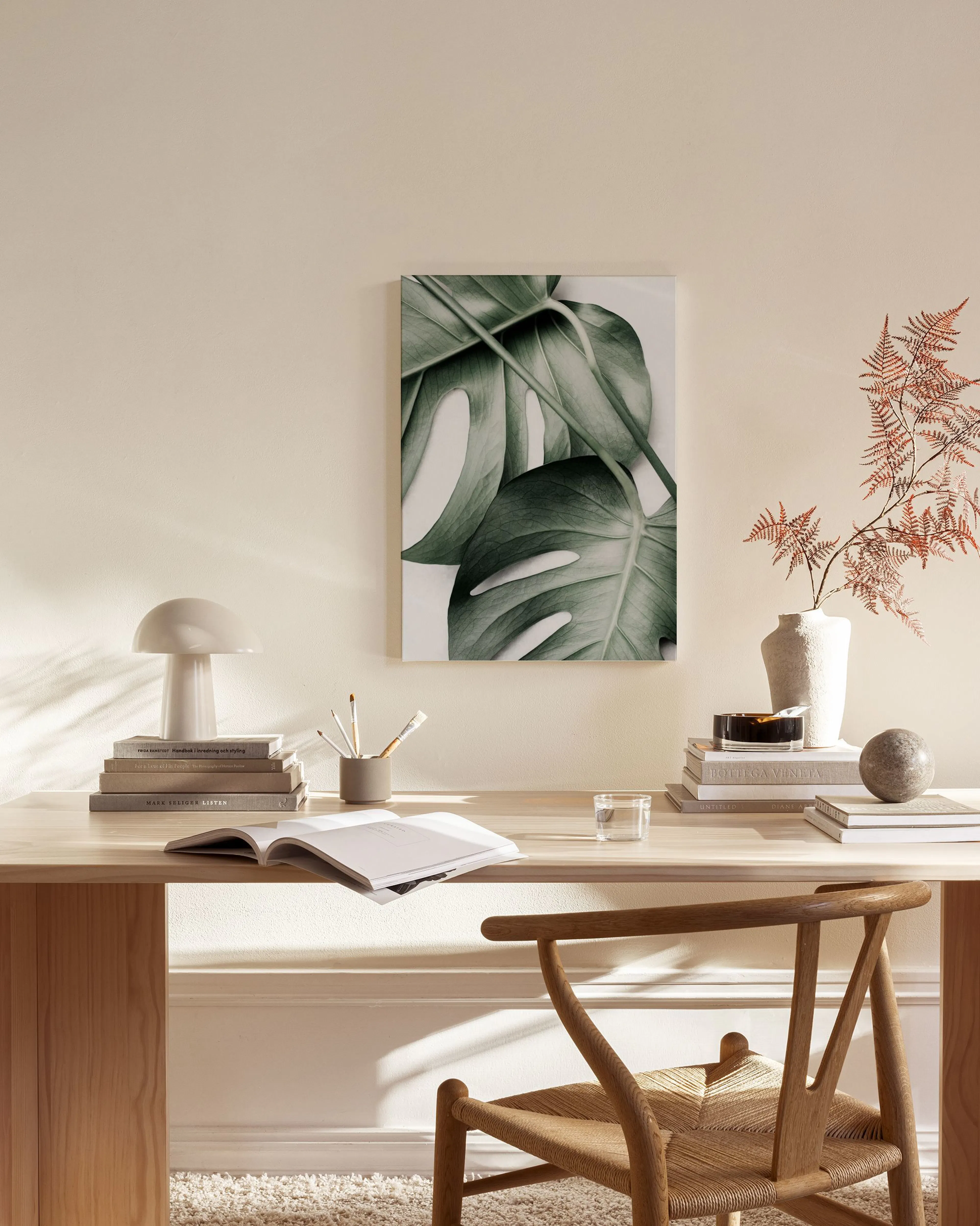 Stampa su tela con foglie di monstera verde scuro, appesa in un moderno soggiorno con mobili in legno chiaro.