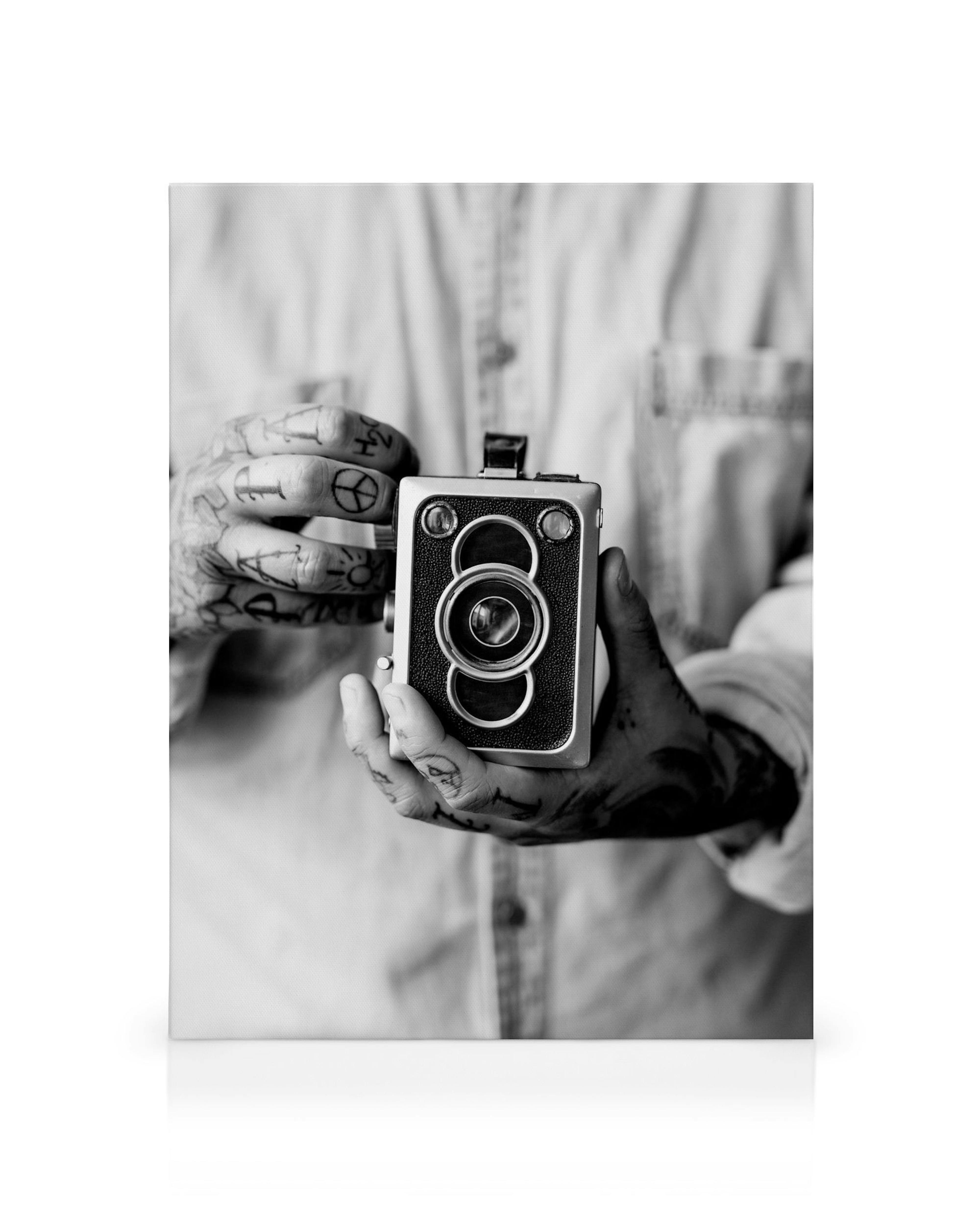 Ασπρόμαυρο φωτογραφικό καμβά με χέρια γεμάτα τατουάζ που κρατούν μια vintage φωτογραφική μηχανή.