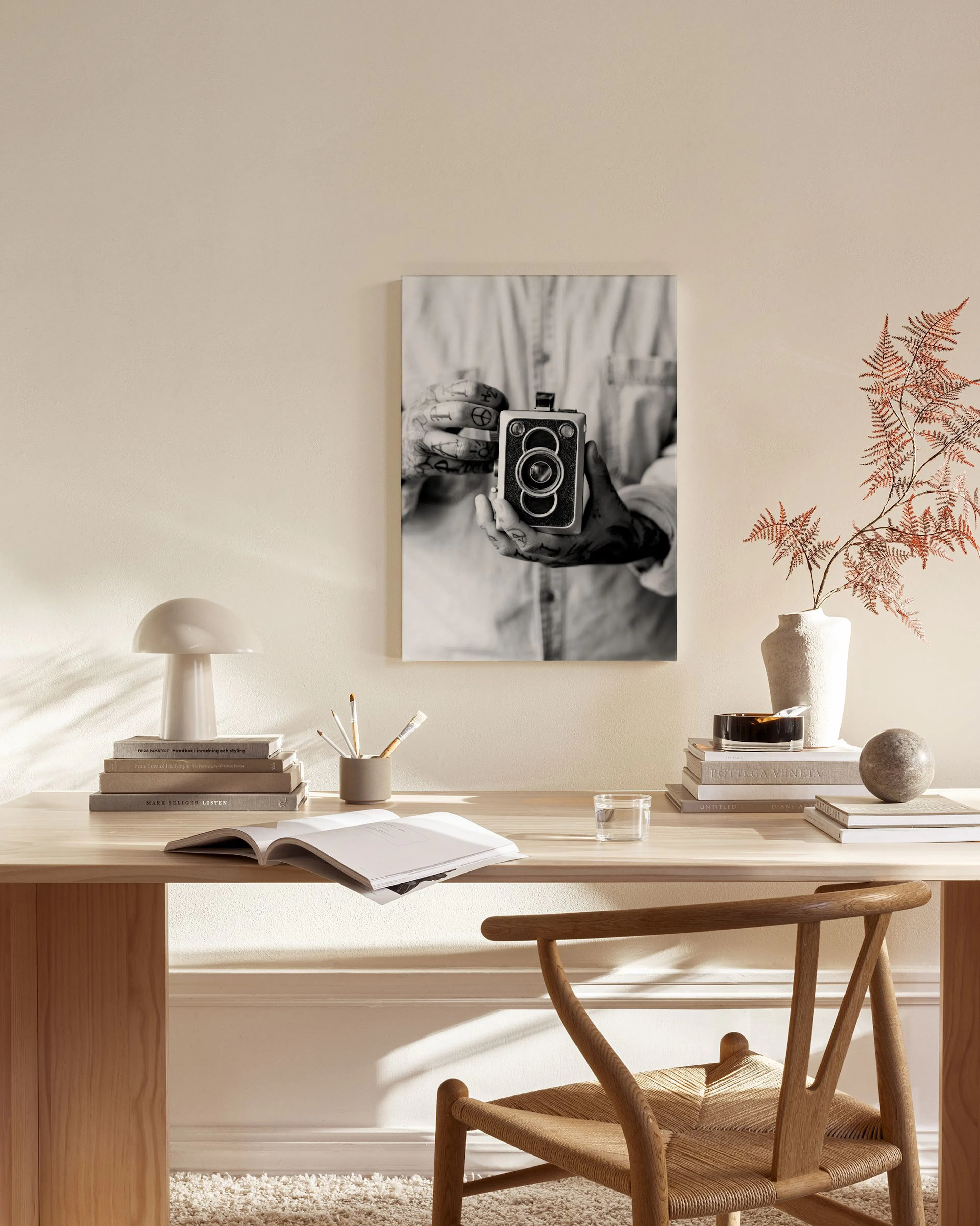 Toile noir et blanc dune personne avec des tatouages tenant un appareil photo vintage, suspendue dans un salon moderne.