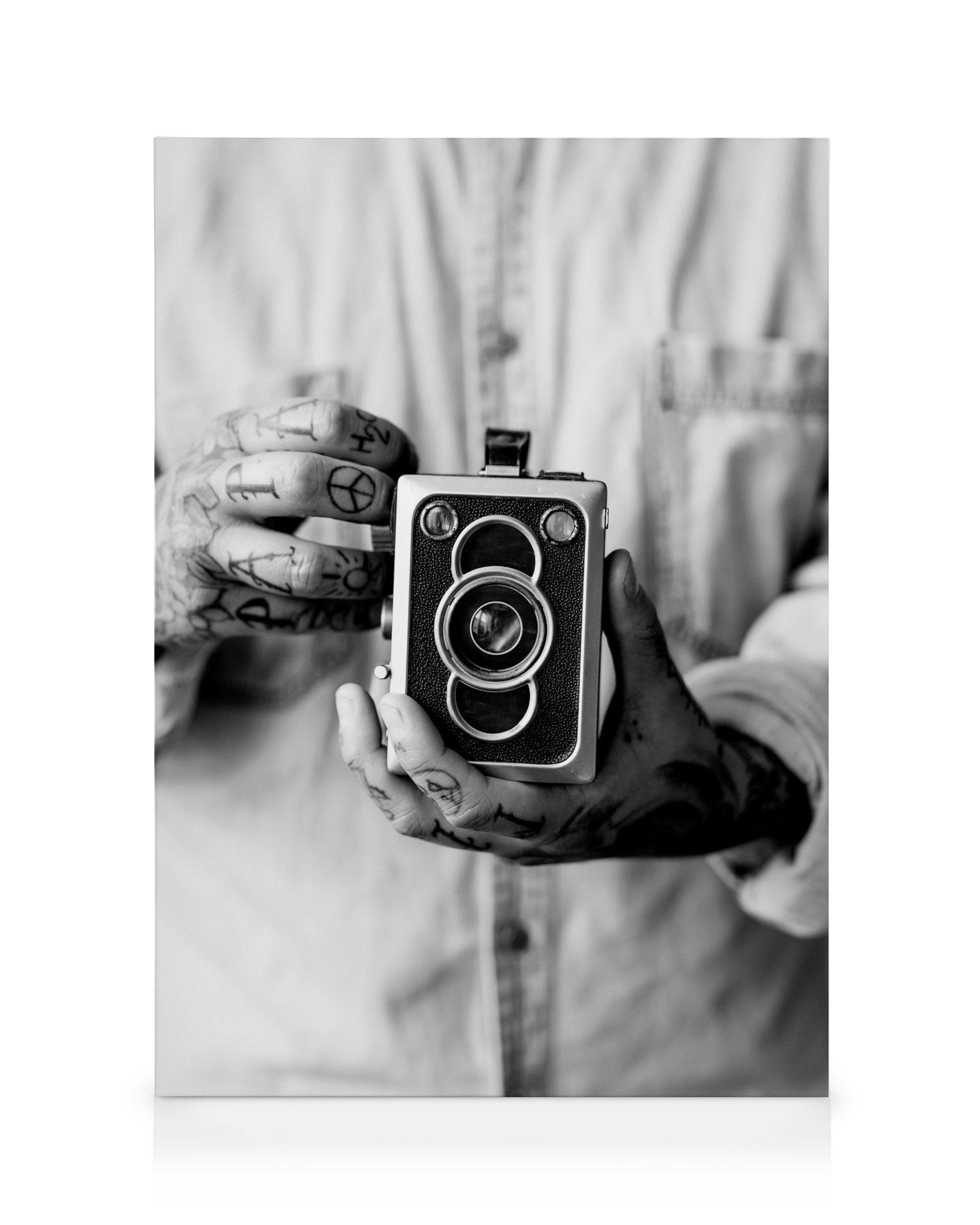 Black and white vintage camera held by tattooed hands, retro photography art on canvas.