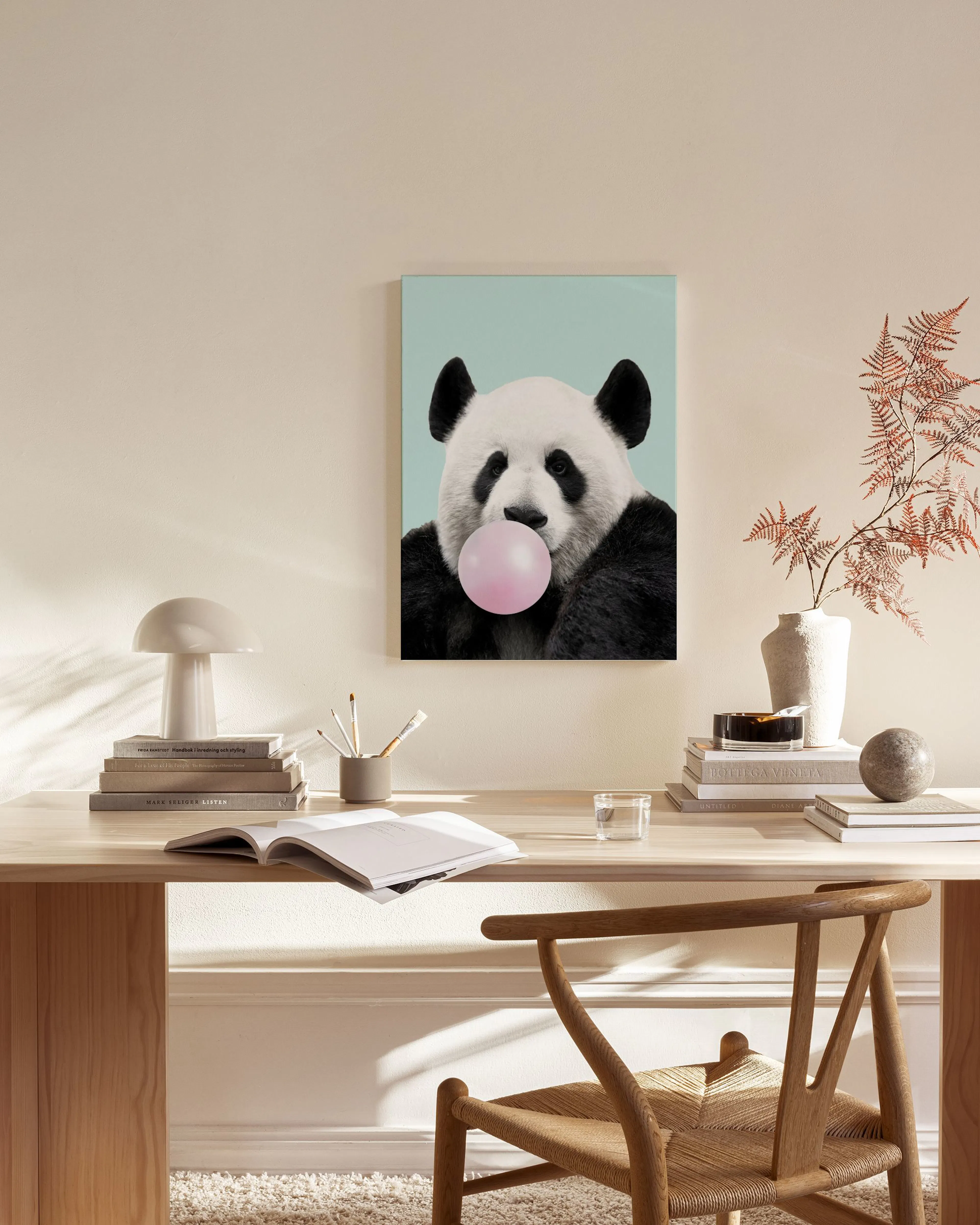 A canvas print of a panda blowing pink bubblegum, displayed above a wooden console table in a minimalist living room.