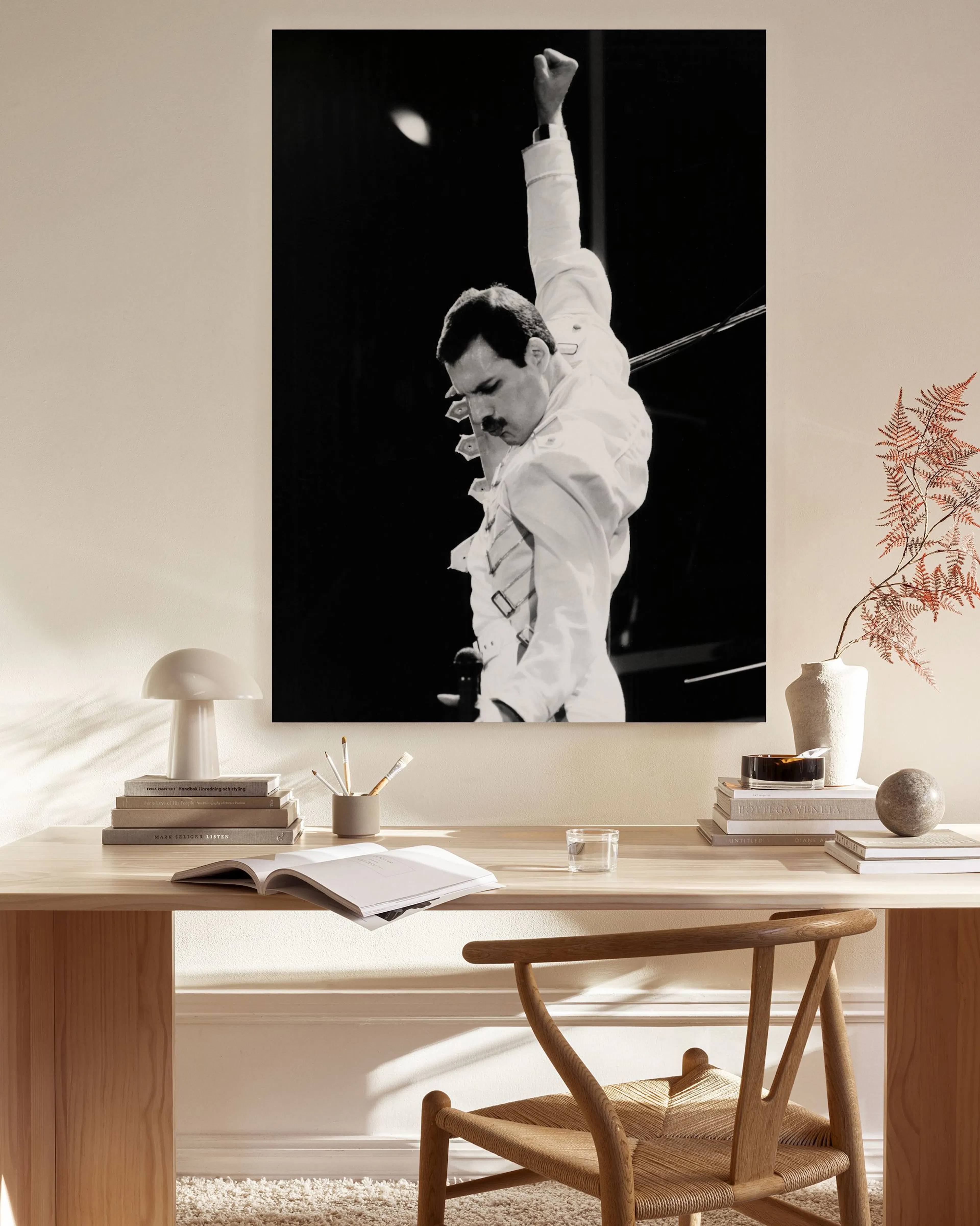 Toile noir et blanc de Freddie Mercury levant le poing, accrochée dans un salon moderne avec fauteuil en bois et table basse.