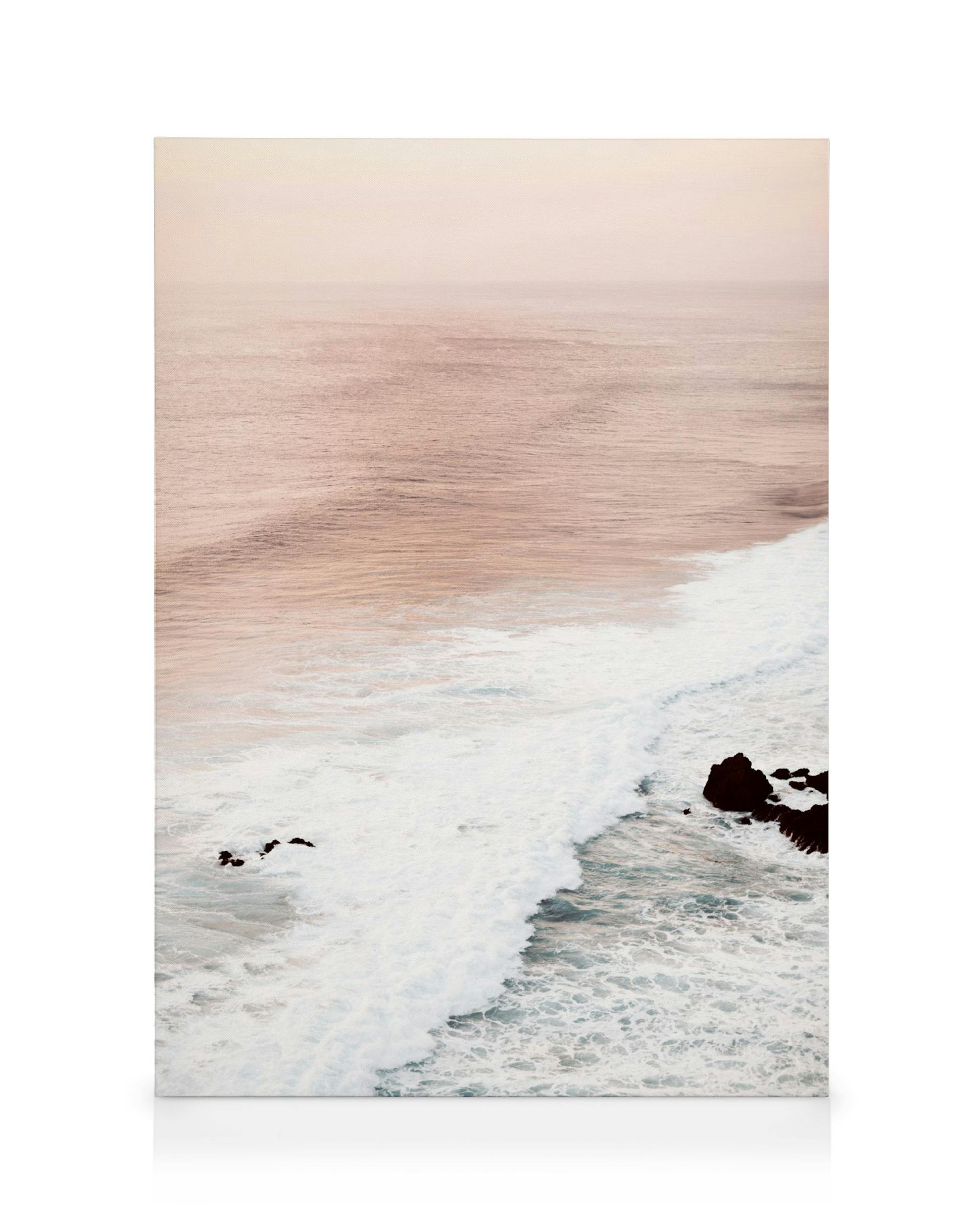 Pastel pink ocean and sky with gentle waves and dark rocks, nature canvas print