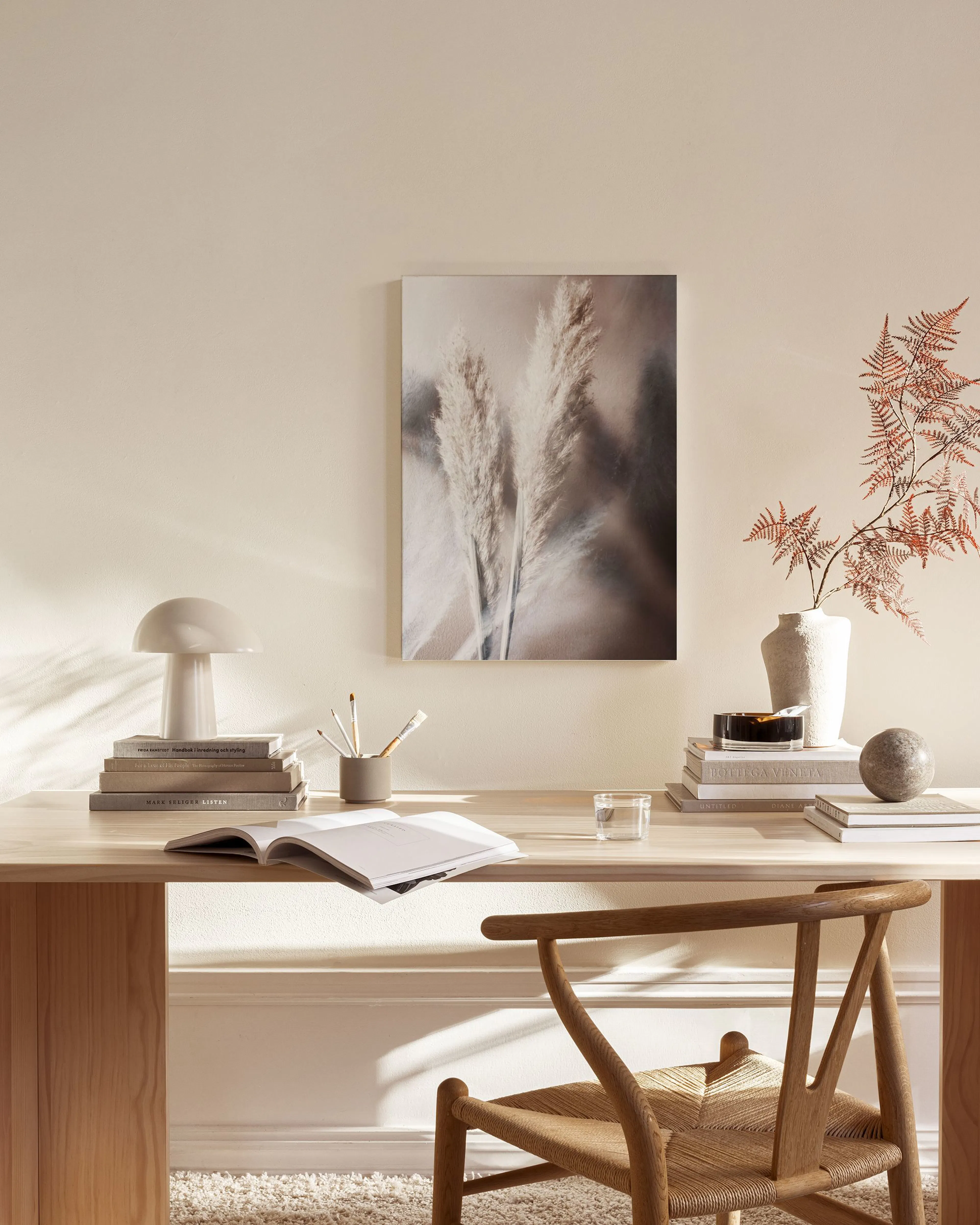 A canvas print of feathery pampas grass with a soft-focus background, hanging above a wooden console table in a minimalist livin