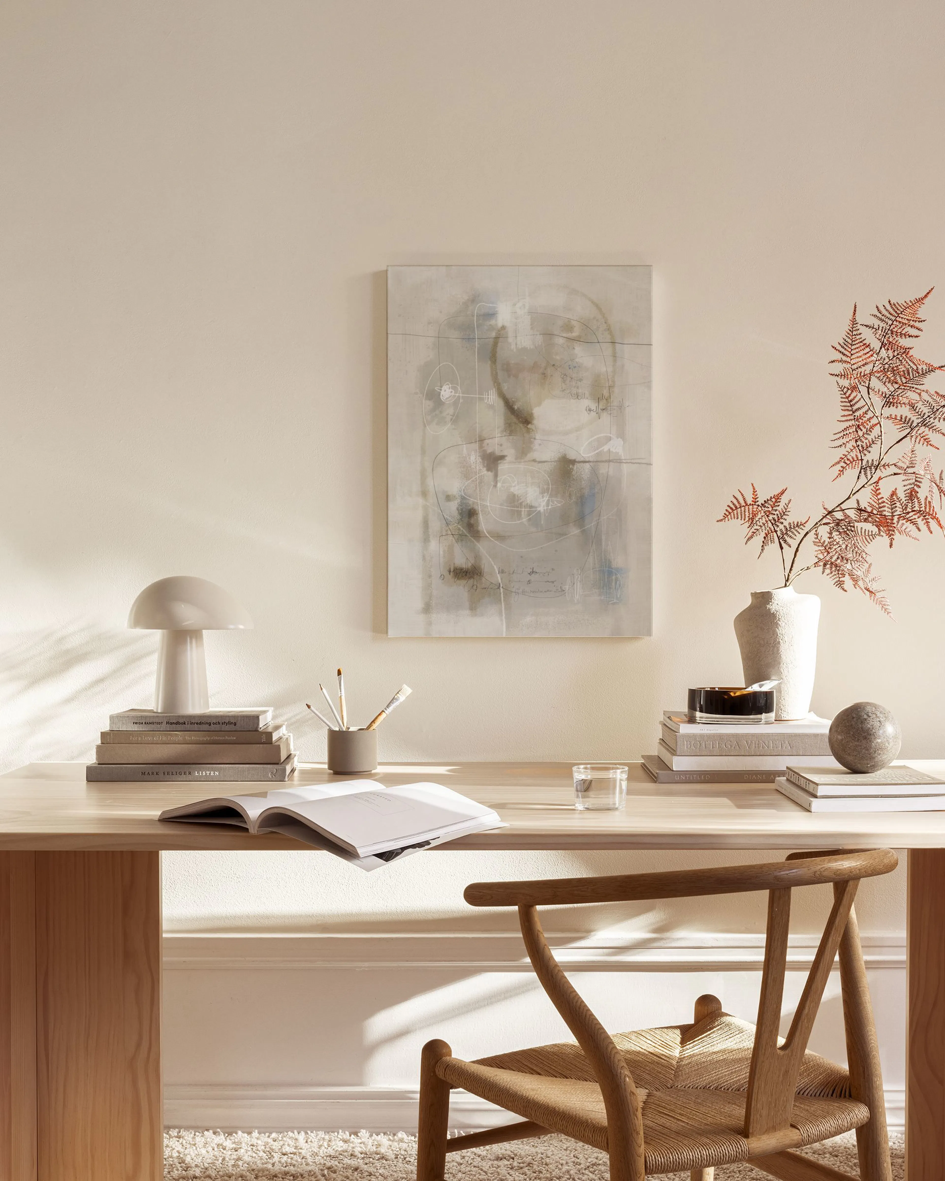 Tela decorativa abstrata com formas orgânicas e linhas brancas, pendurada numa sala de estar minimalista com móveis de madeira c
