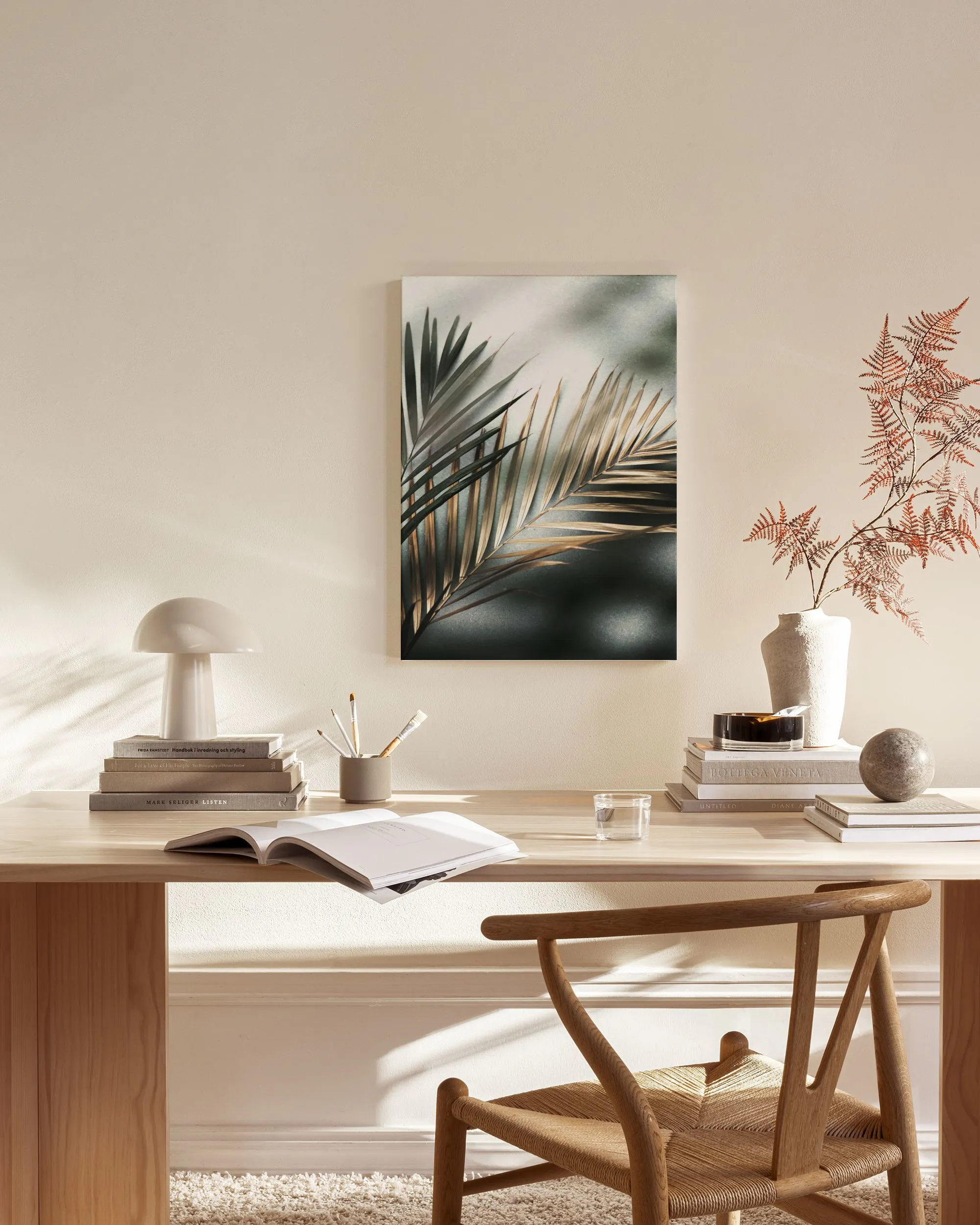 A canvas print of dark green and light brown palm fronds, hanging above a console table in a minimalist living room.